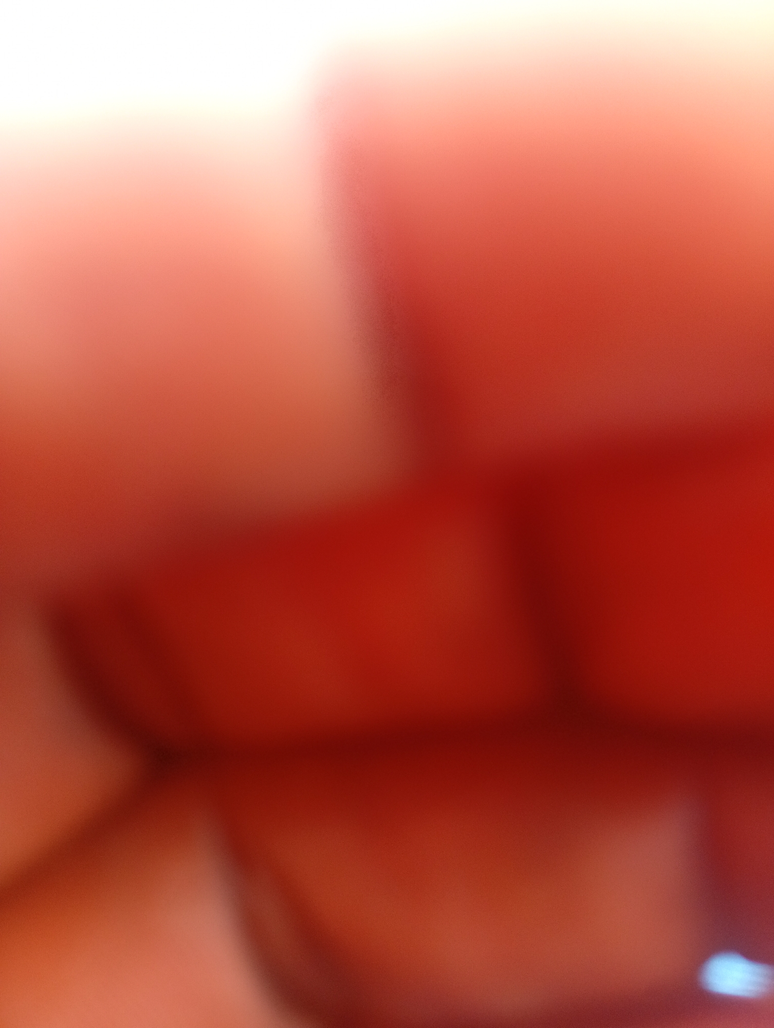 The media file is an abstract, out-of-focus image dominated by shades of red and pink. It appears to be a close-up shot, possibly of human skin or a textured surface reflecting light. There are soft, blurred shapes that suggest form and depth, with lighter areas at the top suggesting a bright light source, perhaps natural daylight. The overall impression is one of warmth and softness due to the color palette and lack of sharp detail. No specific objects, people, or a discernible scene are clearly identifiable. The activity taking place is not evident, and there are no location cues, time of day, or weather indications. No text is visible in the image. The context of Jalingo, Nigeria, does not provide specific visual cues within this abstract imagery.