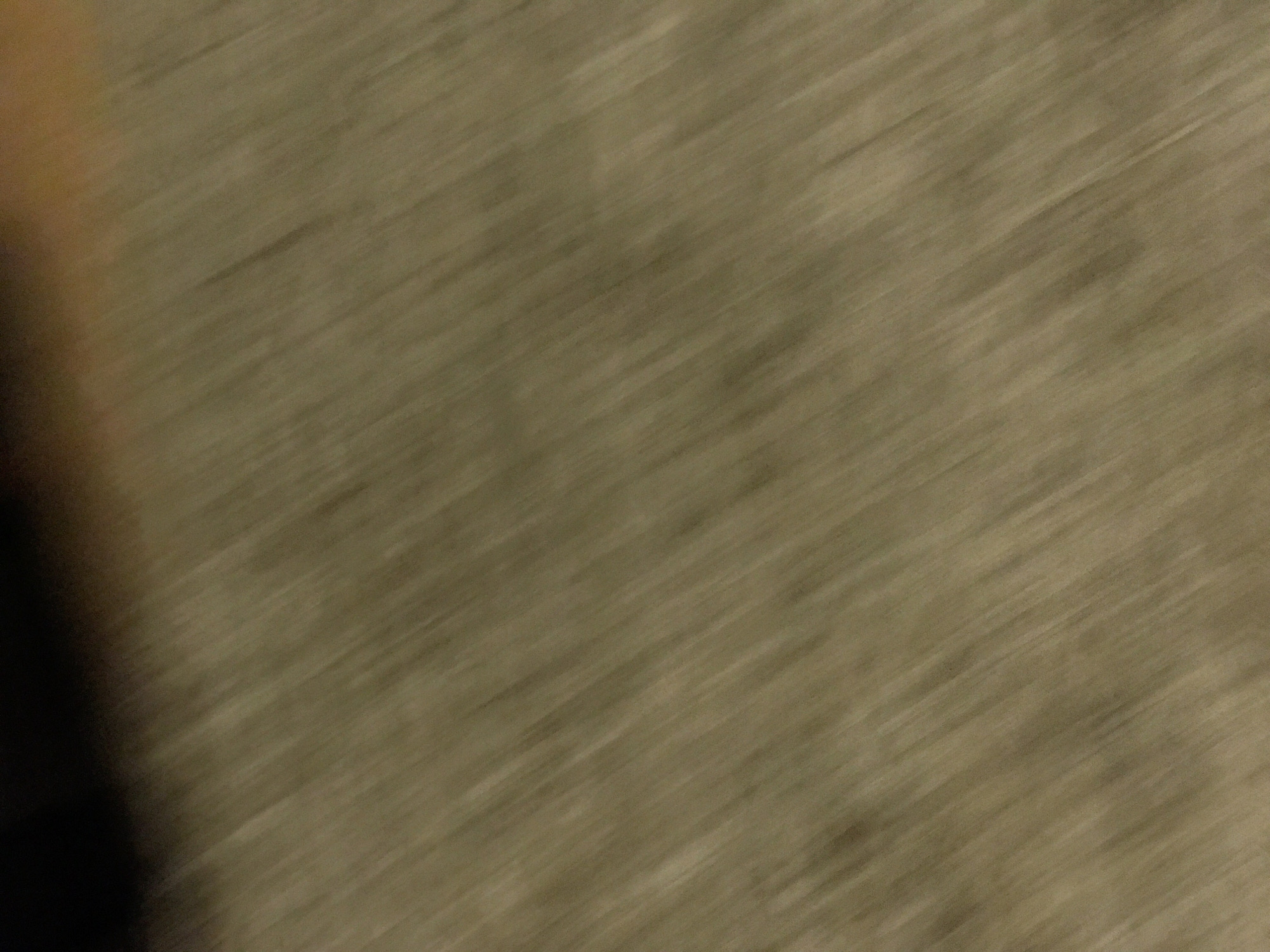 The image is a blurry shot of what appears to be a surface or texture with a predominantly beige or light brown color. The blurriness makes it difficult to discern details, but there are faint indications of subtle patterns or variations in tone. A darker shadow or out-of-focus object is visible on the left side of the image. Without more information, the location in Yerevan, Armenia, cannot be confirmed, and the presence of people, subjects, objects, actions, or interactions is undetectable. The environment is generally unclear due to the motion blur.