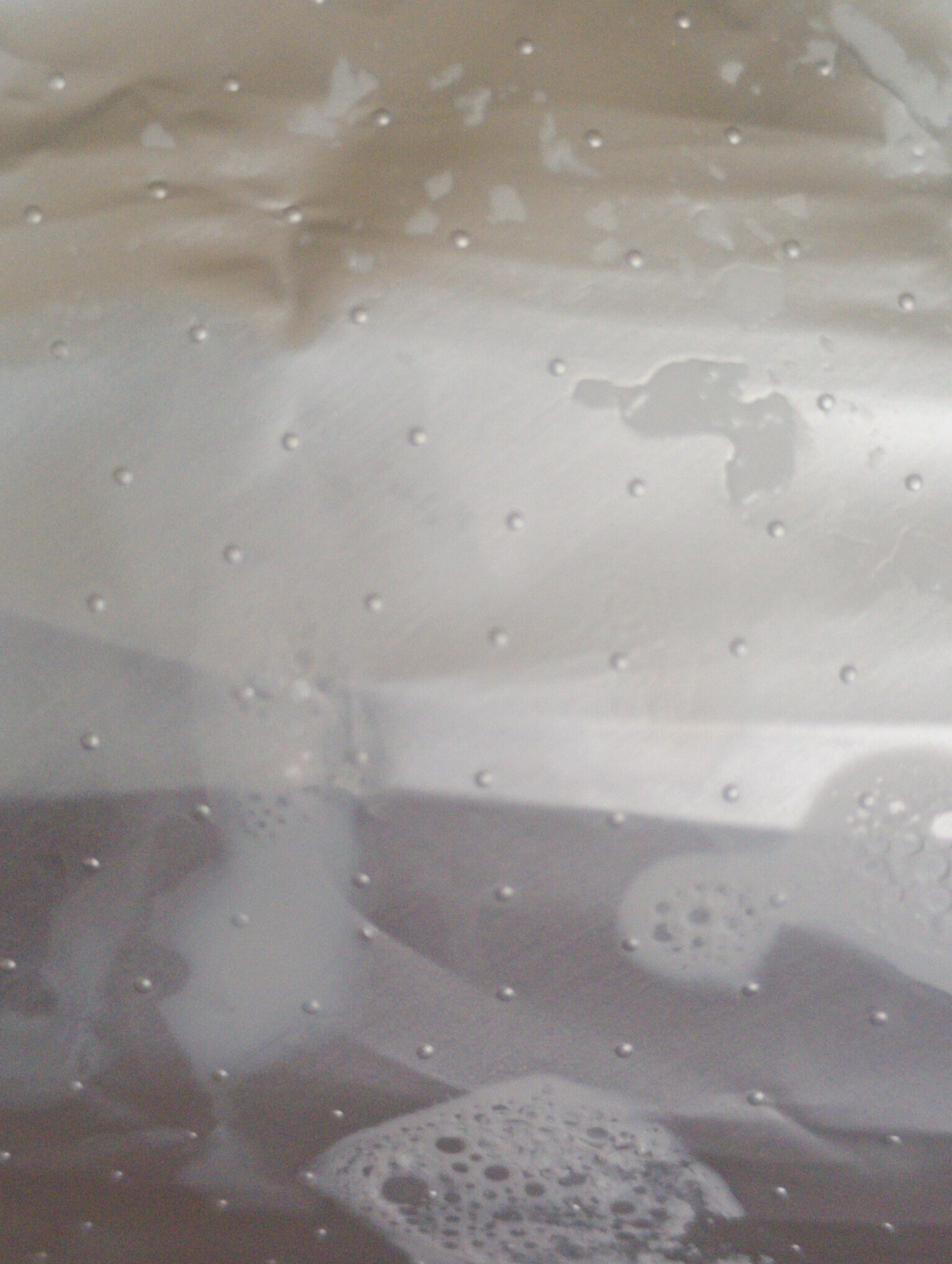 The image shows a close-up of a riveted metal surface. The surface appears to be wet, with water droplets and smears visible. The rivets are small and evenly spaced. The metal surface has varying tones and areas of discoloration. No people, subjects, objects, actions, interactions, or specific environmental elements can be identified within the city of Roza, Bulgaria.