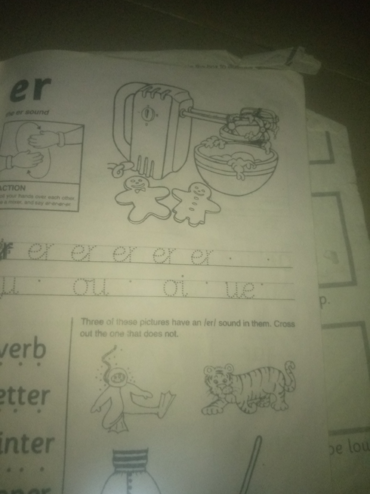 The image depicts a page from a children's educational worksheet. The top section features the letters "er" prominently displayed, followed by "the er sound" and an illustration of a hand mixer with batter and two gingerbread men. Below this, there are lines for tracing the letters "er" and "our" or "ou" and "er". Further down, a sentence reads, "Three of these pictures have an /er/ sound in them. Cross out the one that does not." Two pictures are visible: a diver and a tiger. On the left side of the worksheet, there are words like "verb", "letter", and "winter", with dotted lines for writing practice. The overall setting appears to be an indoor environment, likely a classroom or home, with the worksheet laid out on a surface. There is no information or visual cue in the image to suggest a location in Jauro Yinu, Nigeria.