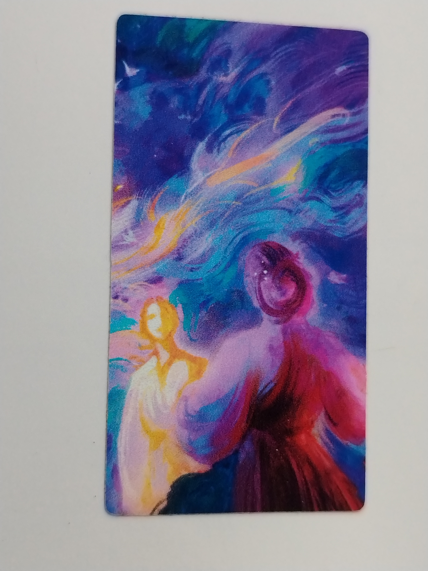 The image is of a rectangular tarot card with rounded corners, set against a plain white surface. The card features a watercolor-style painting. The background of the painting is a blend of deep blues, purples, and hints of turquoise, suggesting a night sky or perhaps a celestial scene. Streaks of yellow and orange are woven throughout the blues and purples, resembling clouds or light rays.
In the foreground, two figures are depicted in a semi-abstract style. On the left, a figure with golden yellow hues is present, their form somewhat vague and ethereal. To the right, a second figure is rendered in shades of red, purple, and pink. The outlines of both figures are indistinct, with colors bleeding and blending into each other, conveying a sense of fluidity and motion.
The scene and subject matter do not contain any information to connect to Izhevsk, Russia.
