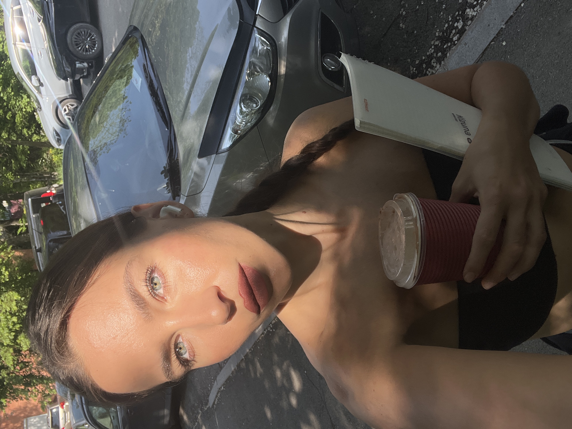 A woman is holding a cup of coffee and a notebook in front of a vehicle. The location is not discernable from the image and therefore it is not possible to confirm the location as Vladivostok, Russia.