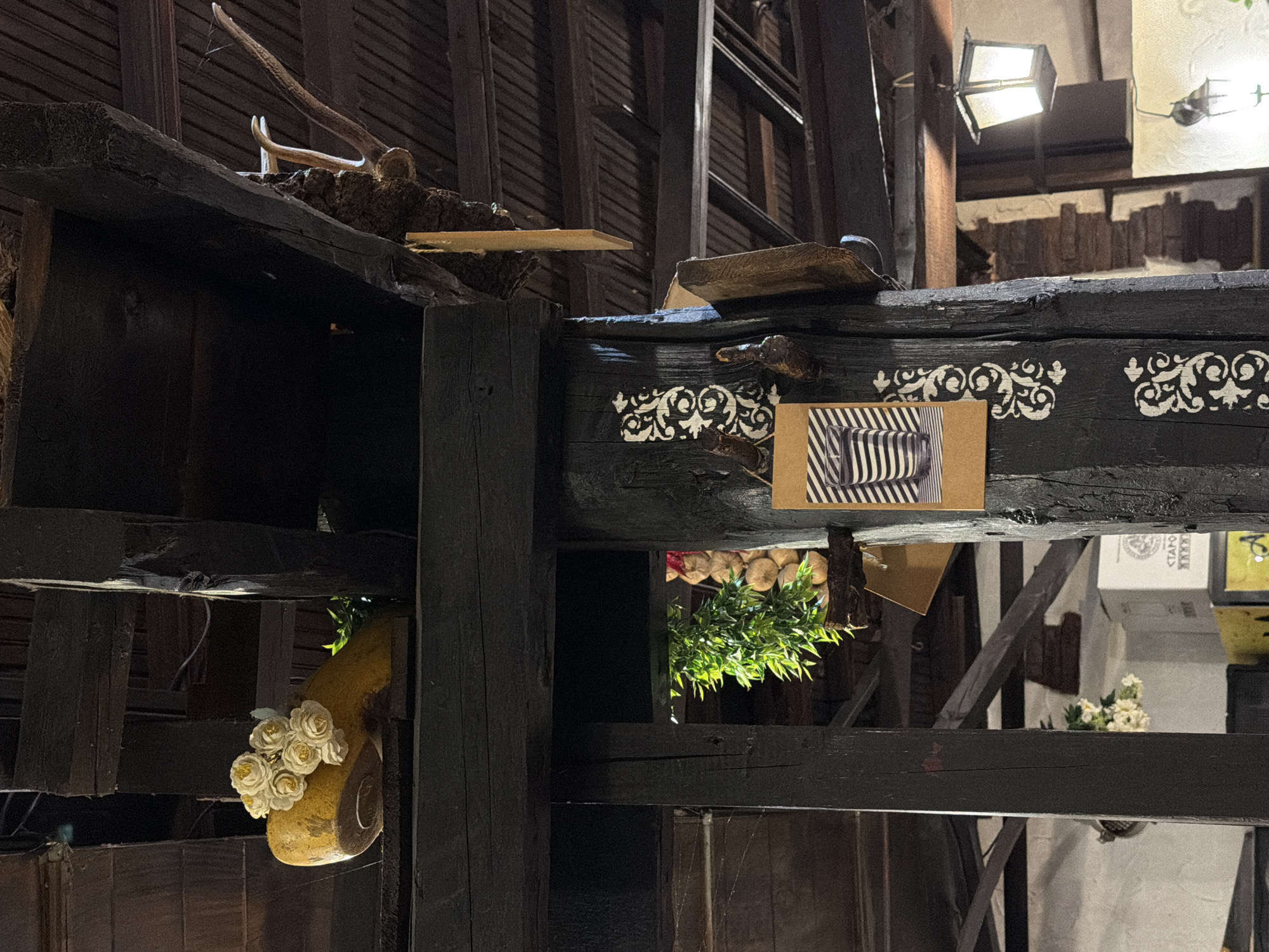The image depicts a dimly lit interior space with rough-hewn wooden beams and structures, likely a restaurant or bar in Varna, Bulgaria. Antlers and other decorative objects are visible. The structural elements and decorations suggest a rustic or historical theme.