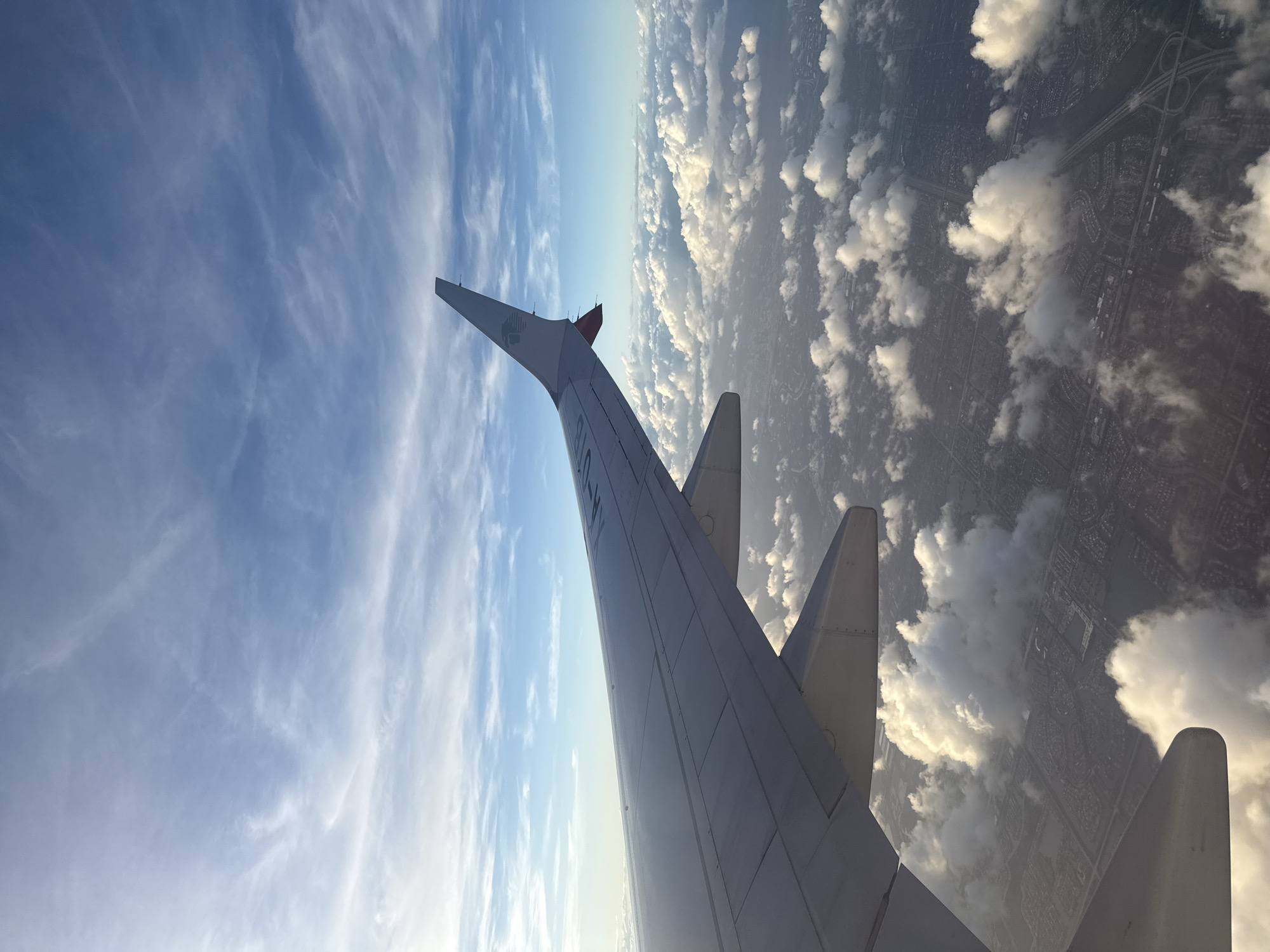 The image shows an airplane wing in flight, with a view of clouds and land below. The wing is white and has a winglet with the logo of the Mexican airline Viva Aerobus. The sky is blue with scattered clouds. Below the clouds, there appears to be a city grid, suggesting an urban area. Based on the presence of Viva Aerobus, the location is likely Mexico City, Mexico, as it is the airline's main hub. The image suggests a flight in or out of Mexico City.