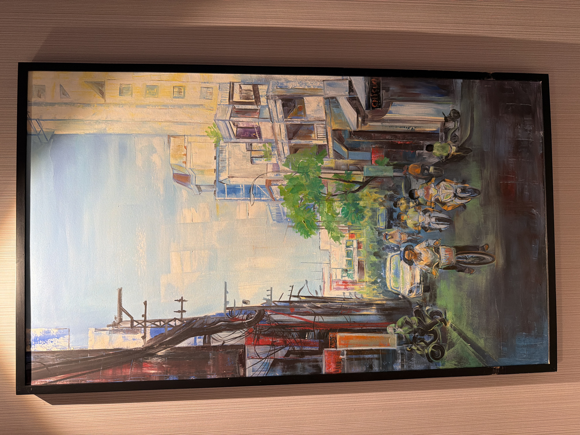 This painting depicts a lively, bustling urban street scene, characteristic of a Vietnamese city like Đà Nẵng. The setting is a narrow thoroughfare lined with multi-story buildings that appear to house a mix of residential and commercial establishments.
The primary subjects are numerous people navigating the street on motorbikes, which are prominently featured. The figures are rendered with expressive, somewhat abstract brushstrokes, capturing movement and presence rather than individual details. At least one larger vehicle, possibly a car or van, is also visible. On the left side of the composition, a dense network of electrical wires and power lines creates a distinctive urban texture. Green trees punctuate the scene, providing splashes of natural color amidst the concrete and asphalt.
The activity taking place is typical daily urban life and commute. The street is crowded with vehicles and people, conveying a sense of constant motion and energy.
Notable details include the clear, bright sky, suggesting a daytime scene. The architecture of the buildings, the prevalence of motorbikes, and the entangled power lines are strong visual cues pointing to a Southeast Asian, specifically Vietnamese, urban environment, aligning with the context of Đà Nẵng. The painting’s style is impressionistic, using visible brushstrokes and a vibrant color palette to evoke the dynamic atmosphere of the city. A faint, indistinct text, possibly "CHI SỐT" or "CHI SUÔT," can be vaguely discerned on a sign on a building in the upper right quadrant of the painting.