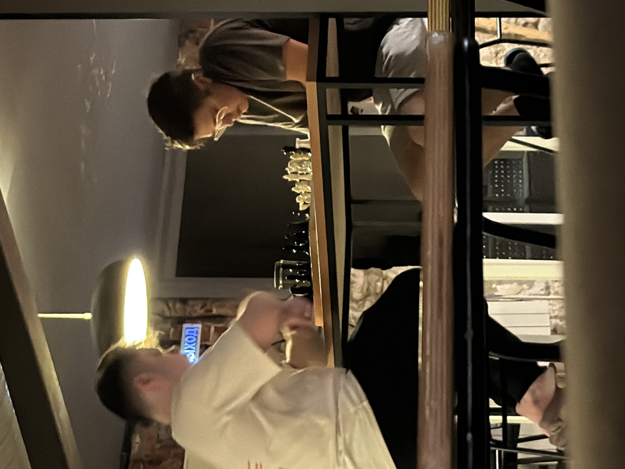 Two individuals are observed in a multi-level interior setting. One person, wearing glasses and a gray shirt, appears to be on an upper level looking down. Another person in a white shirt is on a lower level, looking up. A staircase is prominently featured. In the background, a sign with Cyrillic script, possibly indicating "EXIT" (ВЫХОД), suggests the location is in Russia, and more specifically Moscow. The lighting is somewhat dim.