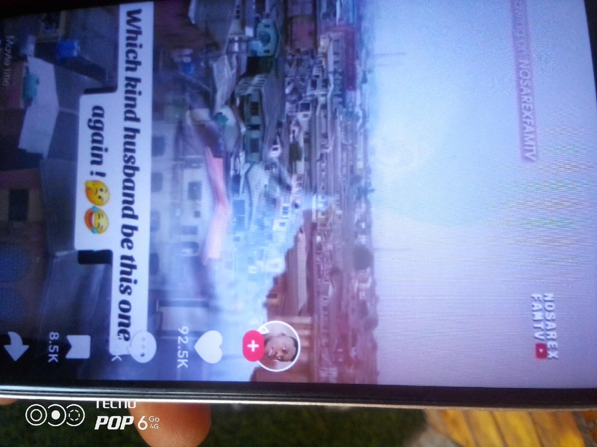 The image displays a TikTok video with vertical text overlay reading "Which kind husband be this one. again!". Below the text, there are two emojis: one with a distressed expression and another with a laughing face. In the lower left, there is an icon indicating 8.5K. To the right, there's a heart icon indicating 92.5K. A circular profile picture with a red plus sign is visible in the center, and a YouTube logo with the text "NOSAREX FAMTY" is in the lower right corner. The background appears to be a cityscape. The phone is identified as a TECNO POP 6 4G. The image quality is poor with visible digital noise and compression artifacts. The location is identified as Howayi, Nigeria through an external source.