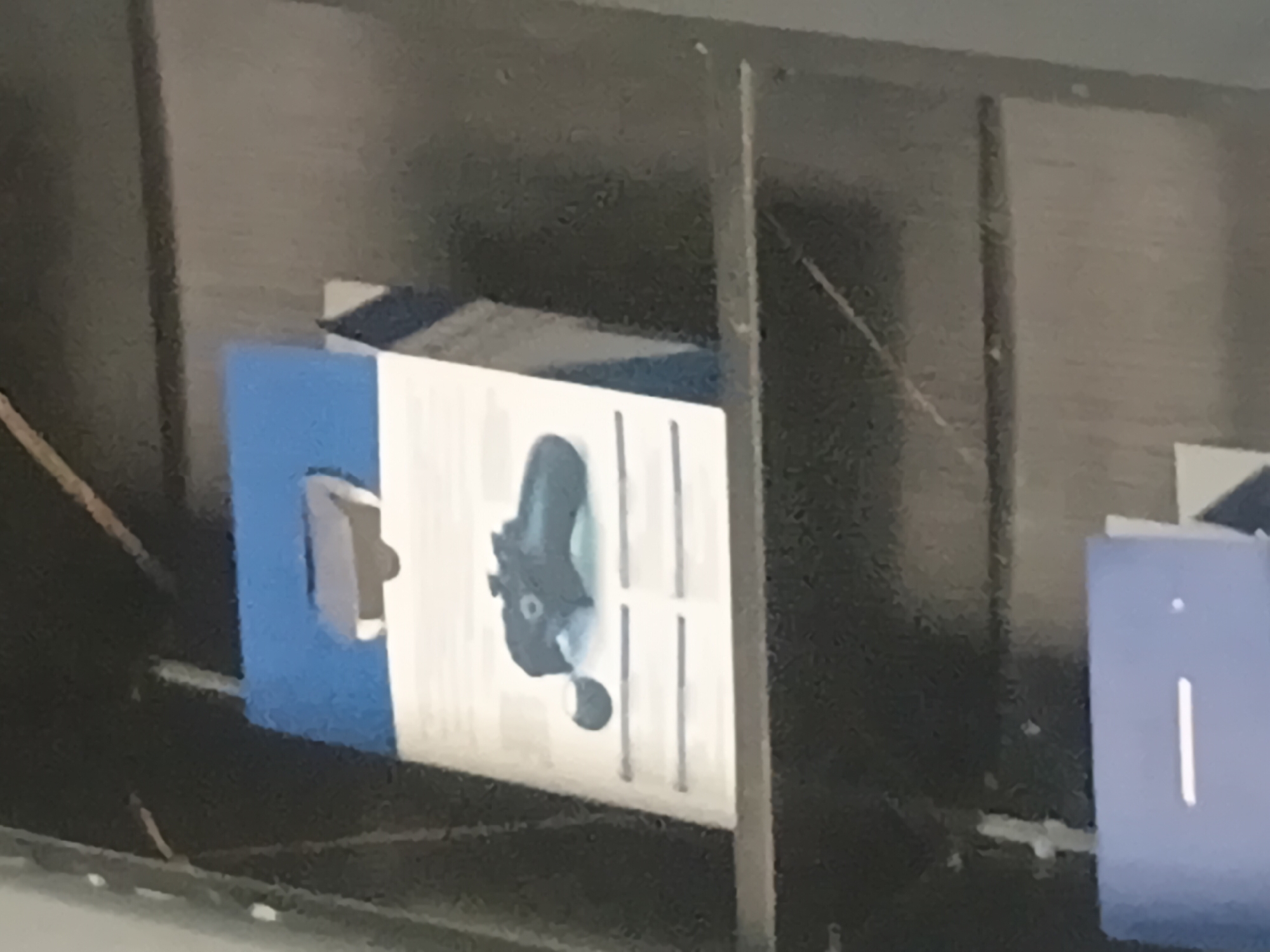 The image shows a close-up of a shelf in what appears to be a retail store. On the shelf is a blue and white box, likely for a gaming controller. A black gaming controller is visible on top of the box, with a small circular accessory beside it. The background is dark and out of focus, suggesting the interior of a store. There are no people or any distinguishing landmarks to indicate the specific location in Jalingo, Nigeria.