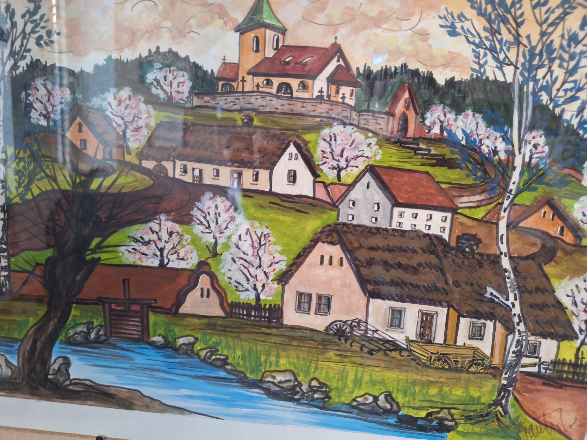 This is a watercolor painting depicting a rural village scene. In the background, a church with a green steeple and red roof sits on a hill, surrounded by trees. In the midground, several houses with thatched roofs and white walls are nestled into a grassy hillside. A stream or river flows in the foreground, with rocks and a tree on its bank. The overall impression is one of a peaceful, idyllic setting. The painting does not depict any people, actions, or interactions. It is a static landscape. The artwork does not offer any specific clues to identify a precise location within Prague, Czechia, as it portrays a generalized rural scene rather than a specific landmark or recognizable urban area.