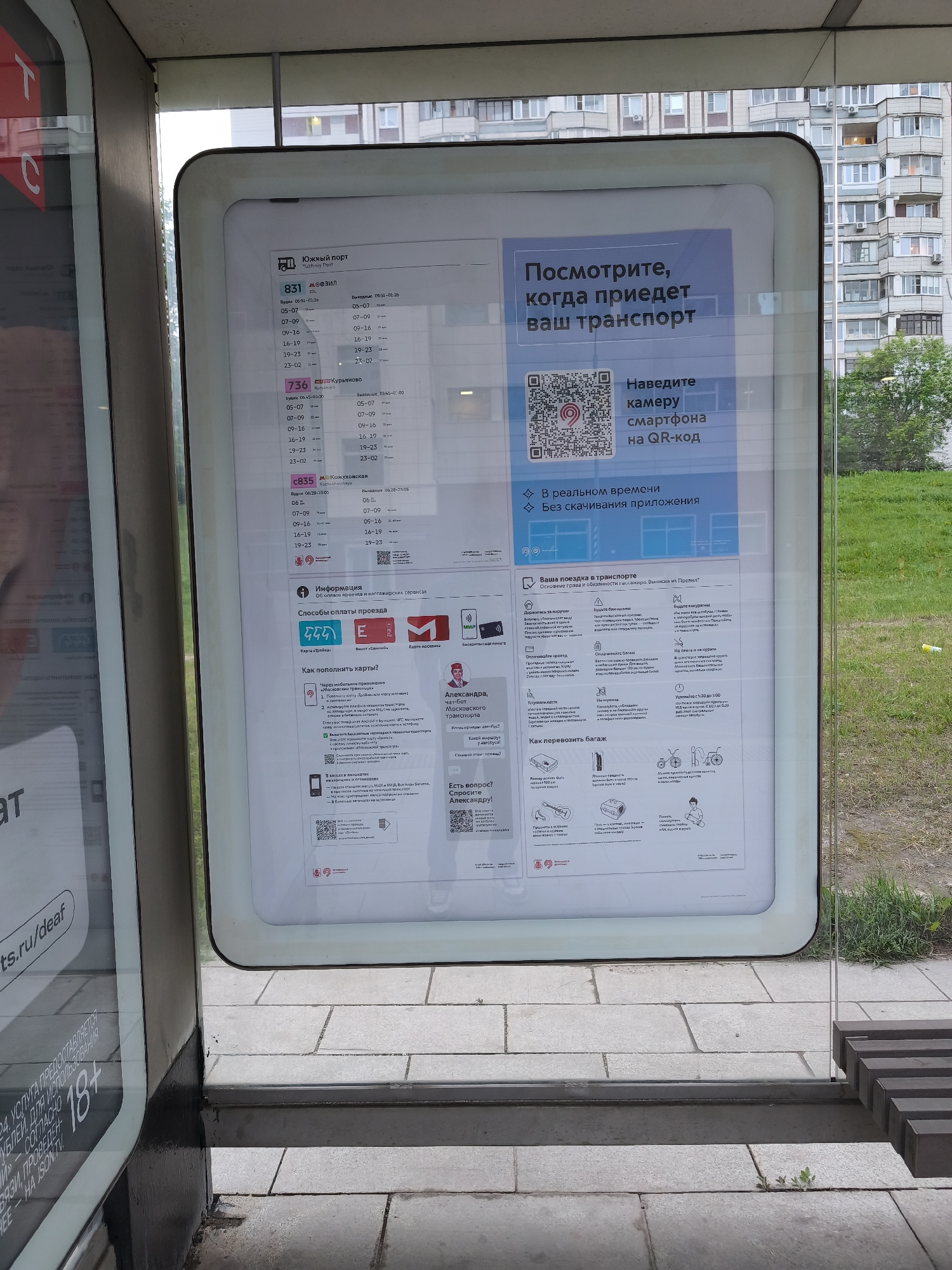The image shows a transit information board located in Moscow, Russia. The board provides details about bus routes (831, 736, c835), schedules, and payment methods. It also contains a QR code for real-time transport updates and information about passenger rights and baggage allowance. The board is situated within a bus shelter, with a glimpse of residential buildings and greenery visible in the background.