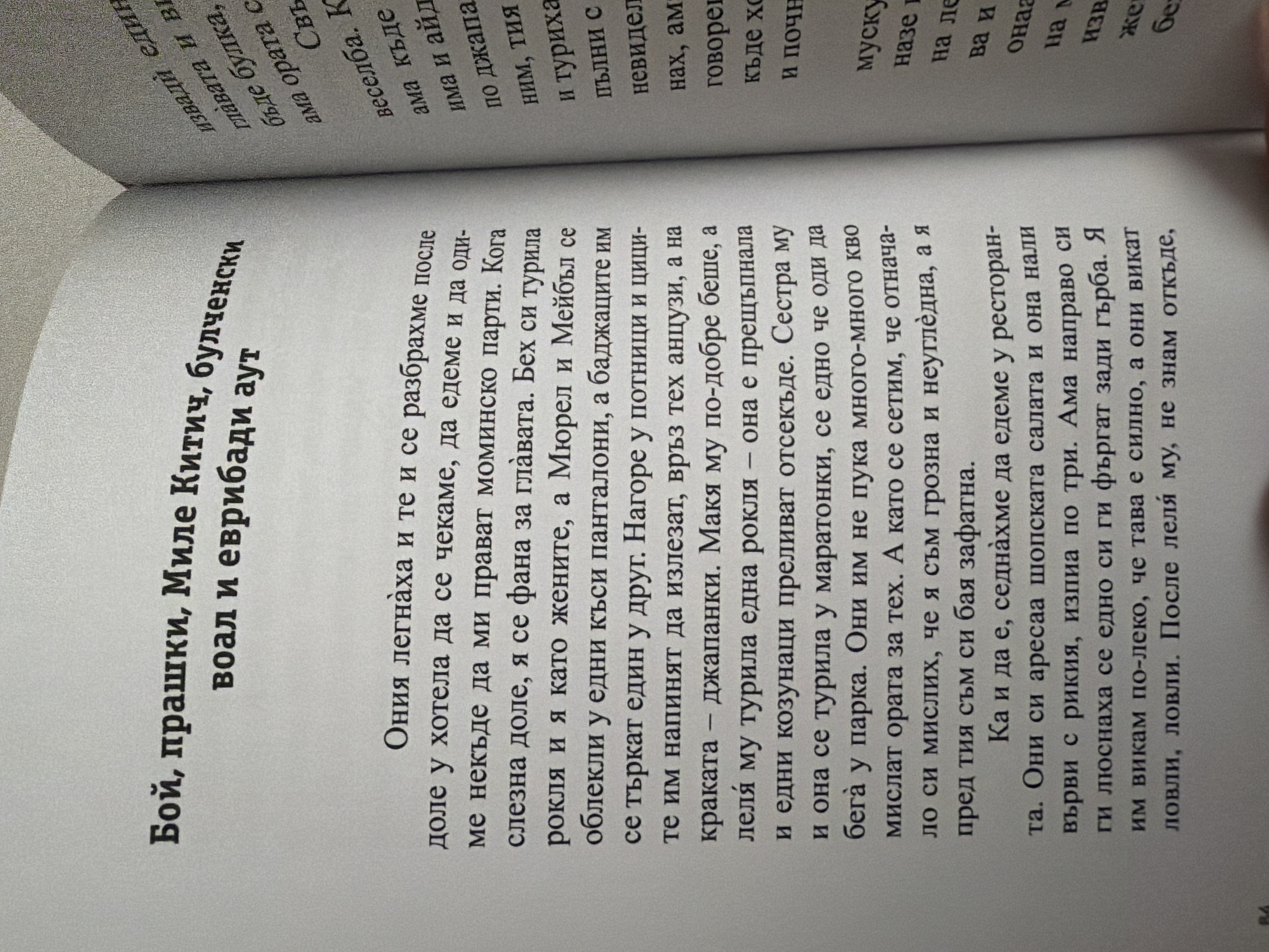 The image shows an open book with two pages of text. The left page has a title in bold: "Бой, прашки, Миле Китич, булченски воал и евриди аут" which translates to "Fight, slingshots, Mile Kitich, wedding veil and evrids out". Below the title is the beginning of a story, with the first paragraph starting with "Ония легнаха и те и се разбрахме после доле у хотела да се чекаме, да едеме и да оди-ме некъде да ми правят моминско парти. Кога слезна доле, я се фана за главата. Бех си турила рокля и я като жените, а Мюрел и Мейбъл се облекли у едни къси панталони, а баджаците им се търкат един у друг. Нагоре у потници и цици-те им напинят да излезат, връз тех анцузи, а на краката – джапанки. Маня му по-добре беше, а леля му турила една рокля – она е прещъпнала и едни козунаци преливат отсекъде. Сестра му и она се турила у маратонки, се едно че оди да бега у парка. Они им не пука много-много кво мислат ората за тех. А като се сети, че отнача-ло си мислих, че я съм грозна и неуглěдна, а я пред тия съм си бая зафатна. Ка и да е, седнахме да едеме у ресторан-та. Они си аресаа шопска салата и она нали върви с рикия, изпипа по три. Ама направо си ги люснаха се едно си ги фъргат зади гърба. Я им викам по-леко, че тава е силно, а они викат ловли, ловли. После леля му, не знам откъде,". The right page contains text in a smaller font, likely a continuation or a different section of the book. The text on the right page begins with "извади един главата и ви бъде булка, ама ората с Свъ веселга. К има къде има и айд по джапа ним, тия и туриха пълни с невидел нах, ам говореи къде хо и почн мускуи назе на ле ва и онаа на м извъ жен бел". The image is a close-up of the pages and does not provide any information about the city of Pazardzhik, Bulgaria, or any specific environmental context beyond being an indoor setting with a book. There are no people or objects visible other than the book itself.