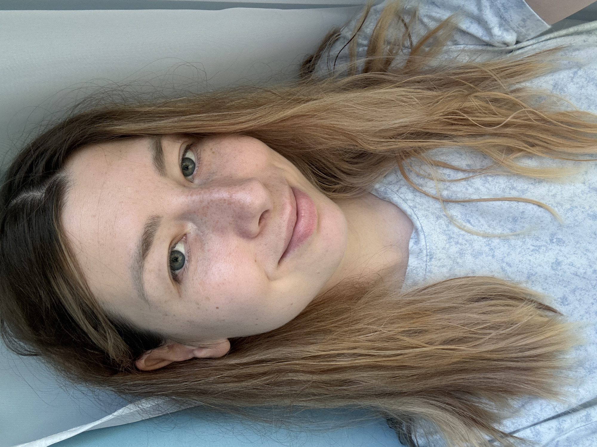 A fair-skinned person with light brown hair lies in what appears to be a bed. The person is wearing a light blue, patterned t-shirt. The setting is indoors, likely a residential bedroom. There is no indication of the location being in Moscow, Russia.