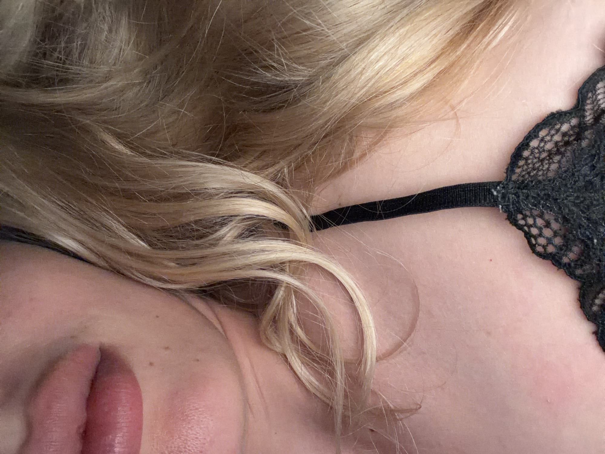 The image shows a close-up of a person with blonde hair. Part of their face, including a portion of their lips, is visible. They are wearing a black lace top. The location in Budva, Montenegro is not discernible from the image.
