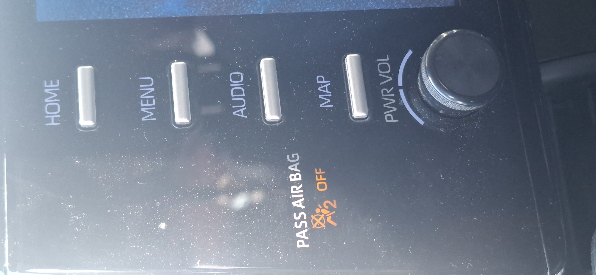 A car's infotainment system display is visible, showing several buttons and a warning light. The buttons are labeled "HOME," "MENU," "AUDIO," and "MAP." Below the "PASS AIR BAG" text, there is an illuminated orange symbol indicating the passenger airbag is OFF. A large, circular knob labeled "PWR VOL" is at the bottom of the display, likely for power and volume control. The dashboard is dark and has a matte finish, with specks of dust visible on the screen. The background is blurred, suggesting the image was taken from inside a vehicle. The specific city in Israel is not discernible from the image.