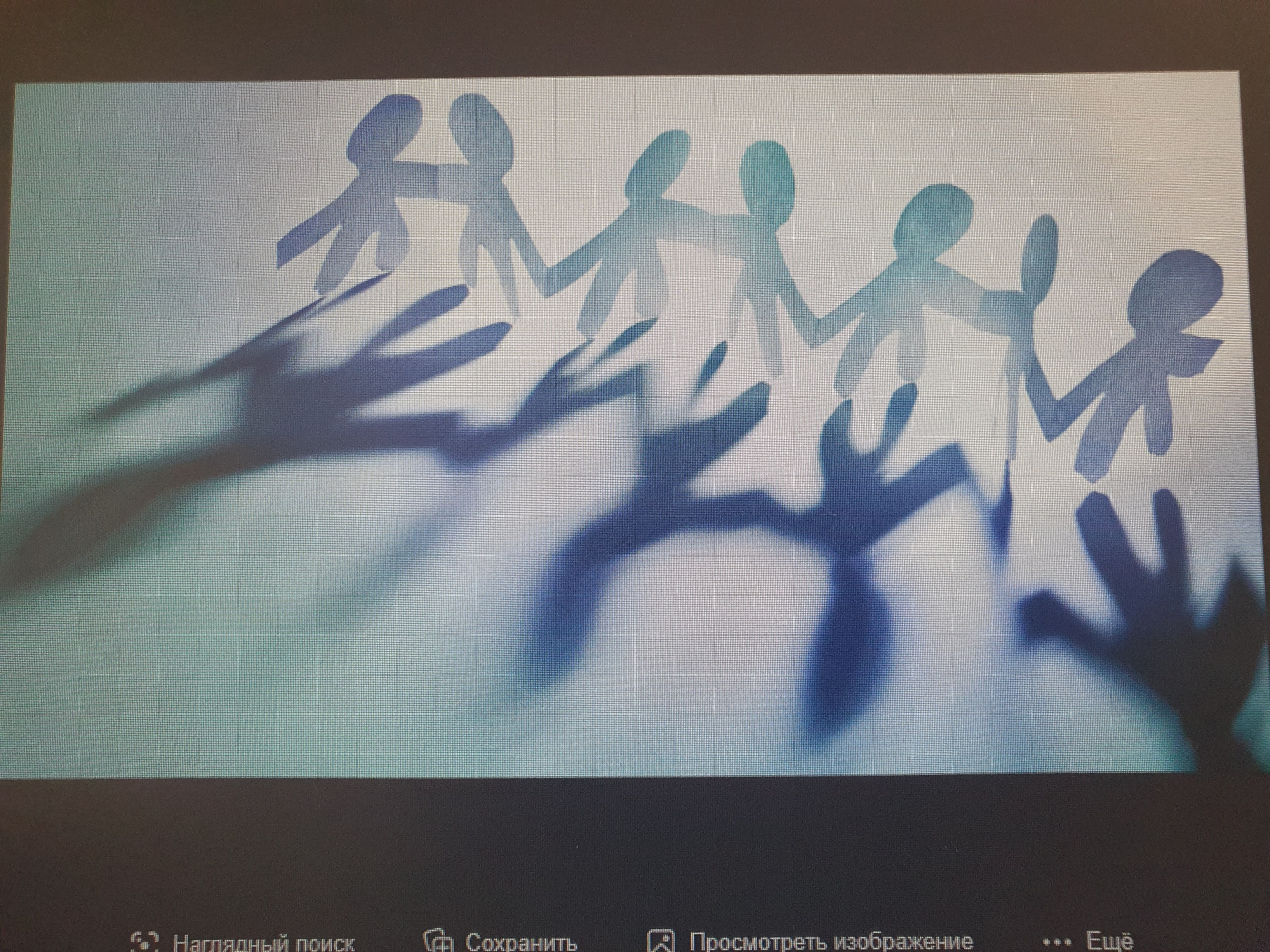 The image shows a light-colored textured surface illuminated from the left, casting elongated shadows of paper cutouts of several human figures. The figures are linked hand-in-hand and appear to be in a line or chain, with their arms outstretched. The shadows are a deep blue and purple, creating a stark contrast with the bright white background. The figures themselves are also white, with some subtle blue and green gradients, suggesting they are lit from the side and back. The overall impression is one of unity and connection, represented by the chain of figures. The bottom of the image shows a dark bar with some text in Russian, indicating it is a screenshot from a computer interface, and there is no indication of the image being taken in Tashkent, Uzbekistan.