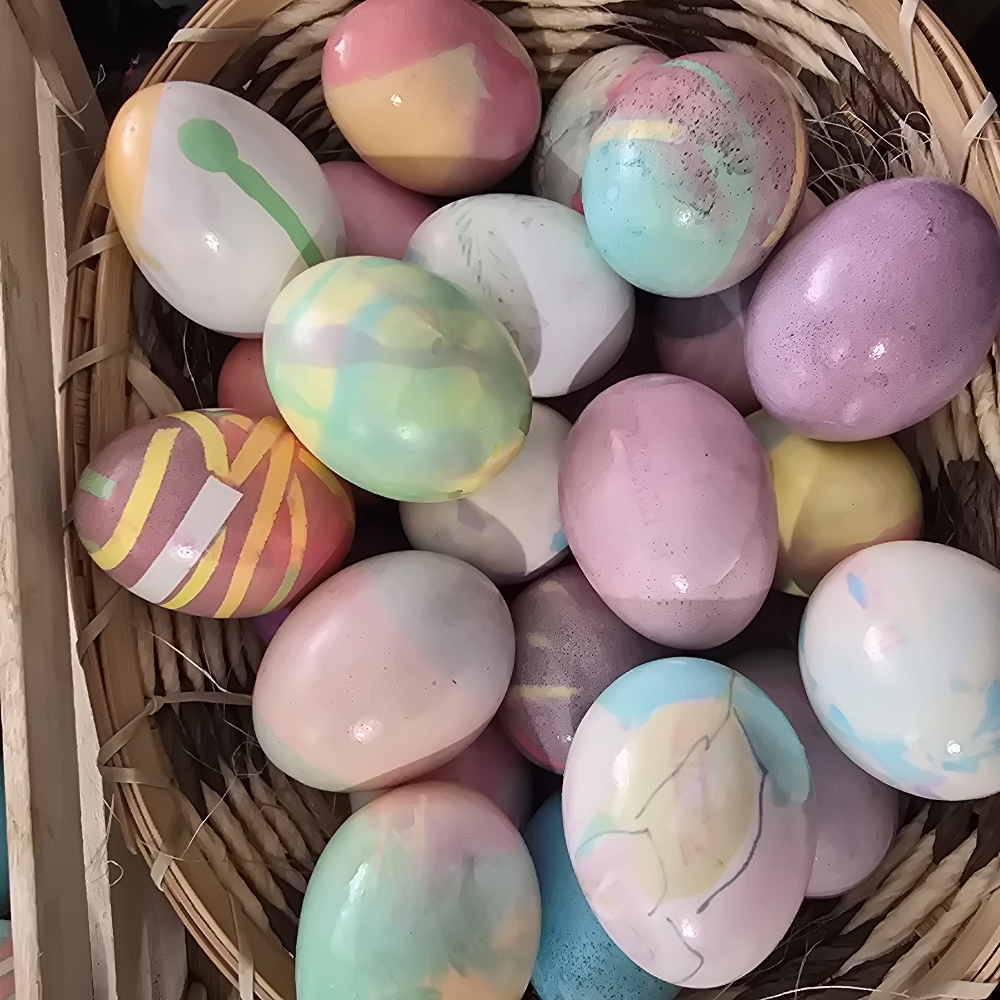 A basket filled with decorated Easter eggs is the primary focus. The eggs have various pastel colors and designs. The basket is made of woven material. The scene appears to be indoors, possibly in Plovdiv, Bulgaria, if it is related to an Easter celebration there.