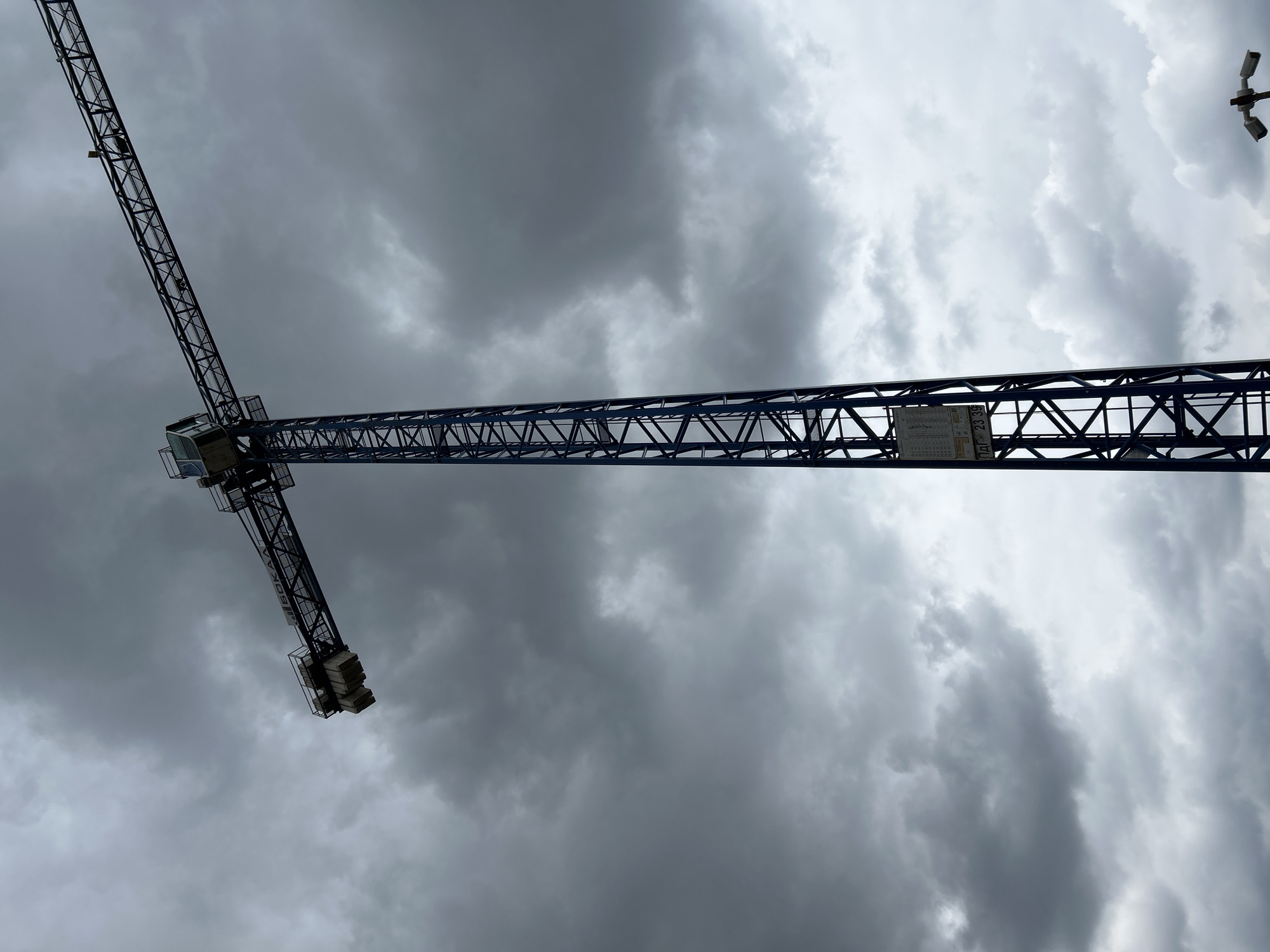 A low-angle shot shows a blue construction crane against a stormy sky in Sofia, Bulgaria. The crane's jib extends horizontally across the frame. In the upper right corner, a bird is flying.