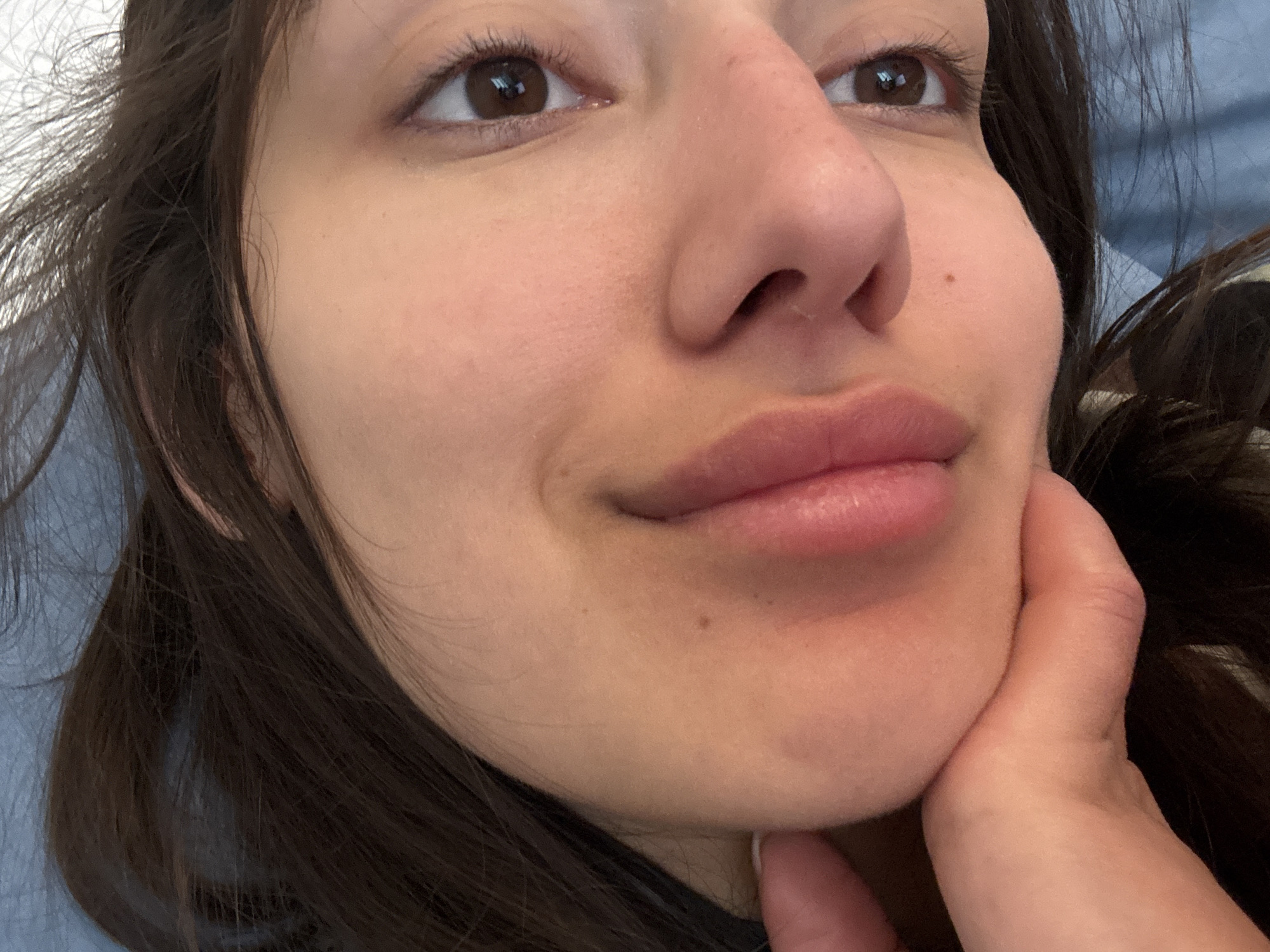 A close-up photograph depicts the face of a young woman with brown hair. Her face is fair, and she has brown eyes. Her right hand is positioned under her chin, slightly obscuring her neck. The background appears to be a soft, muted blue fabric. There is no indication of the city of Zankovići, Montenegro, within the visible content of the image.