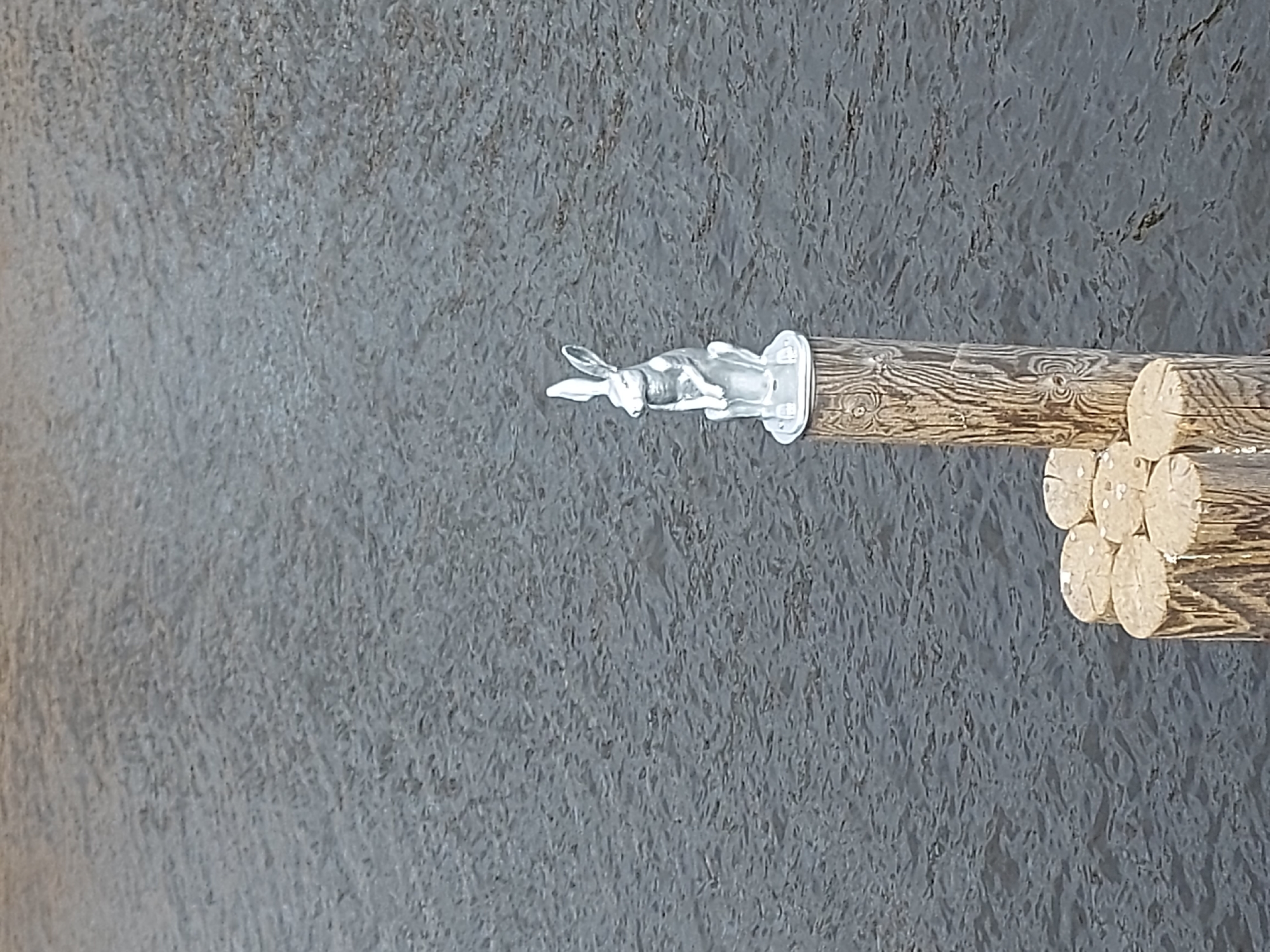 The image shows a clear glass rabbit figure mounted on a wooden stick, likely a decorative or souvenir item. The background is a textured, gray surface, possibly a stone wall or pavement. Without further context, it's impossible to confirm the exact location in Saint Petersburg, Russia, or if the image was taken there. No people or actions are visible.