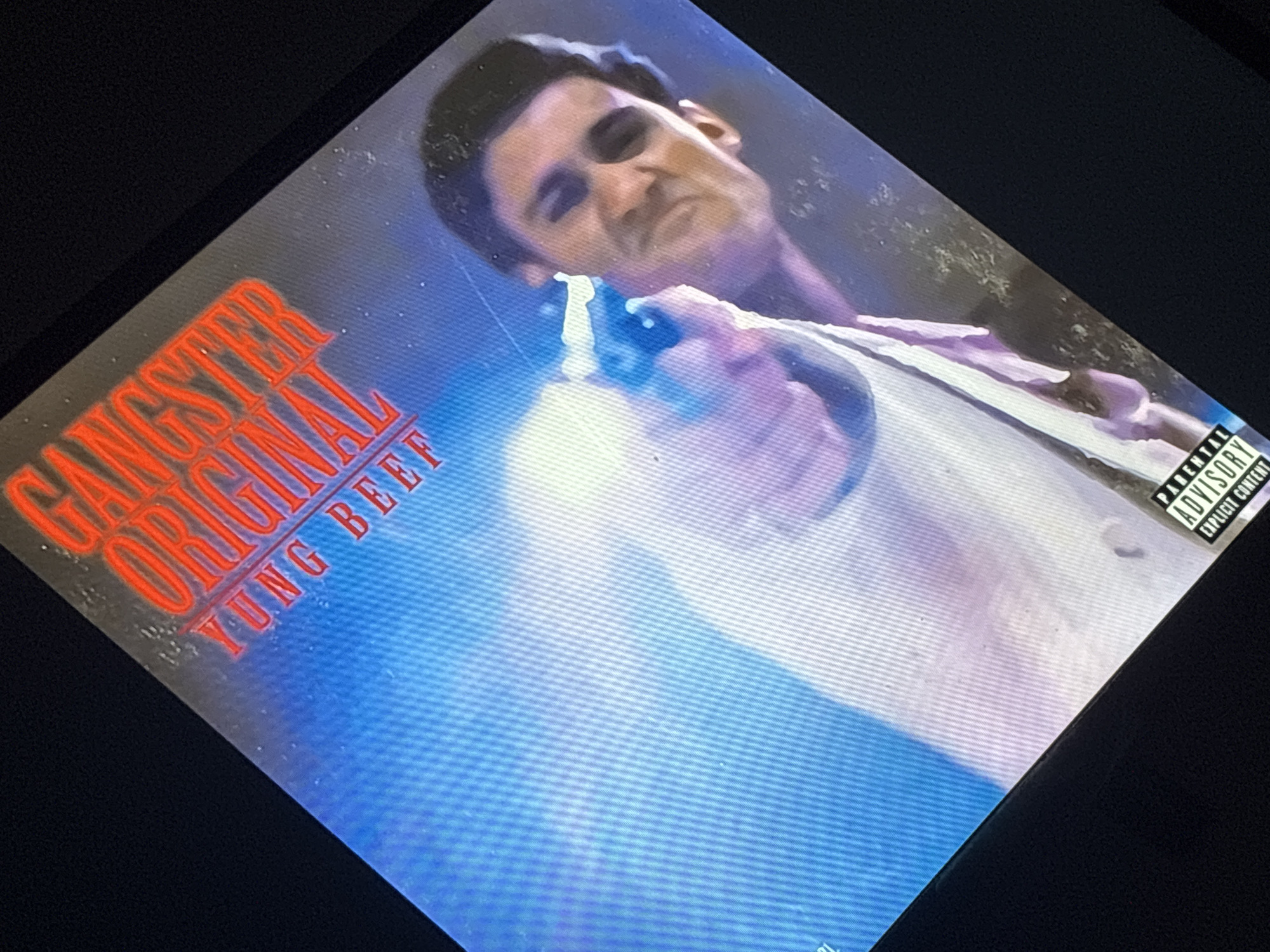 The image is an album cover with the words "GANGSTER ORIGINAL YUNG BEEF" in red text. A man is pointing a gun, and the album has a "Parental Advisory" label. I do not see any indication of this being in Buenos Aires, Argentina.