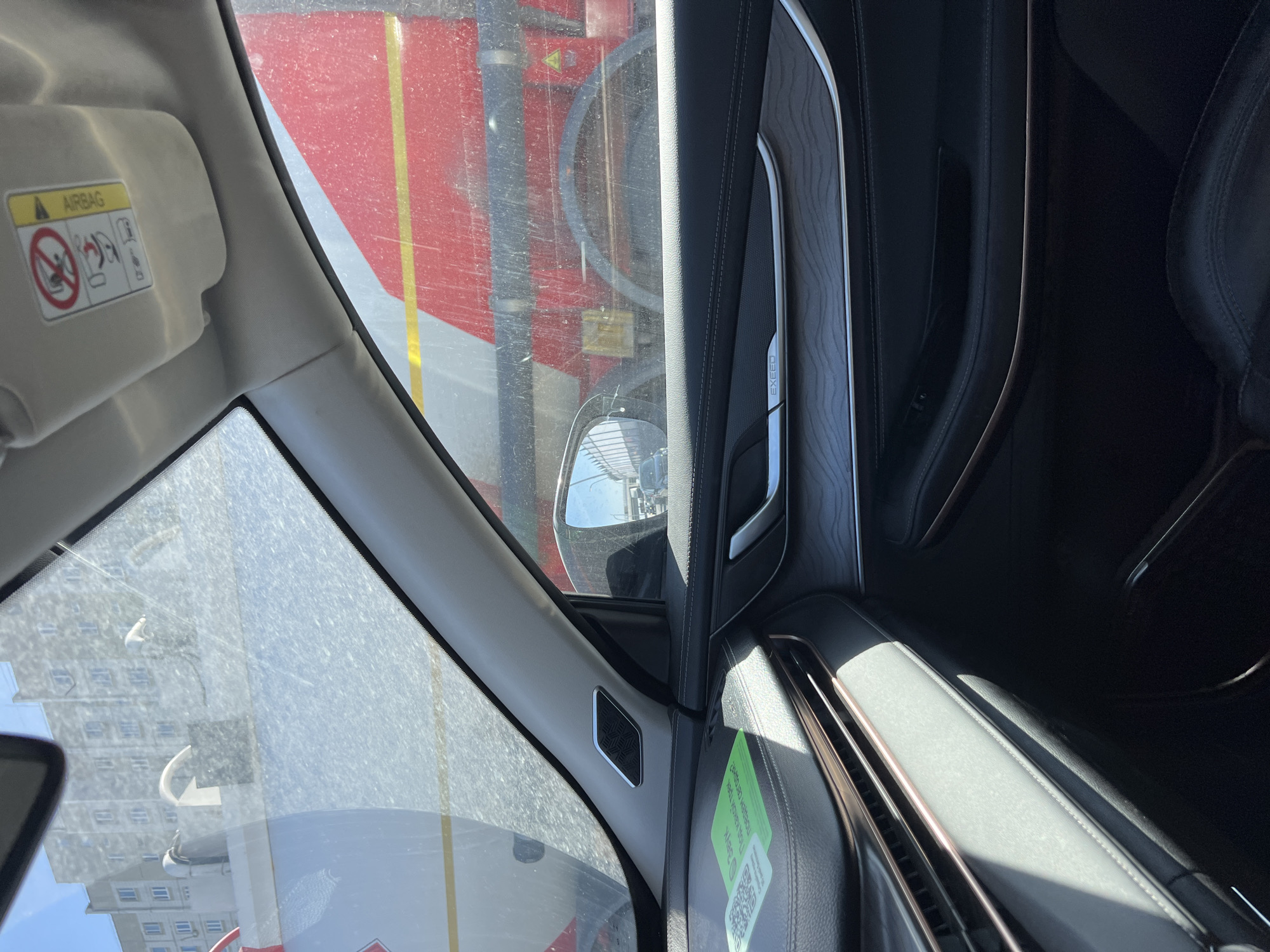 The view from inside a car shows the exterior of what appears to be an airport building in Moscow, Russia. The window view is somewhat obstructed by a dirty windshield. The wing of the car is visible and the interior view captures parts of the car's interior including the door with the Exeed logo.