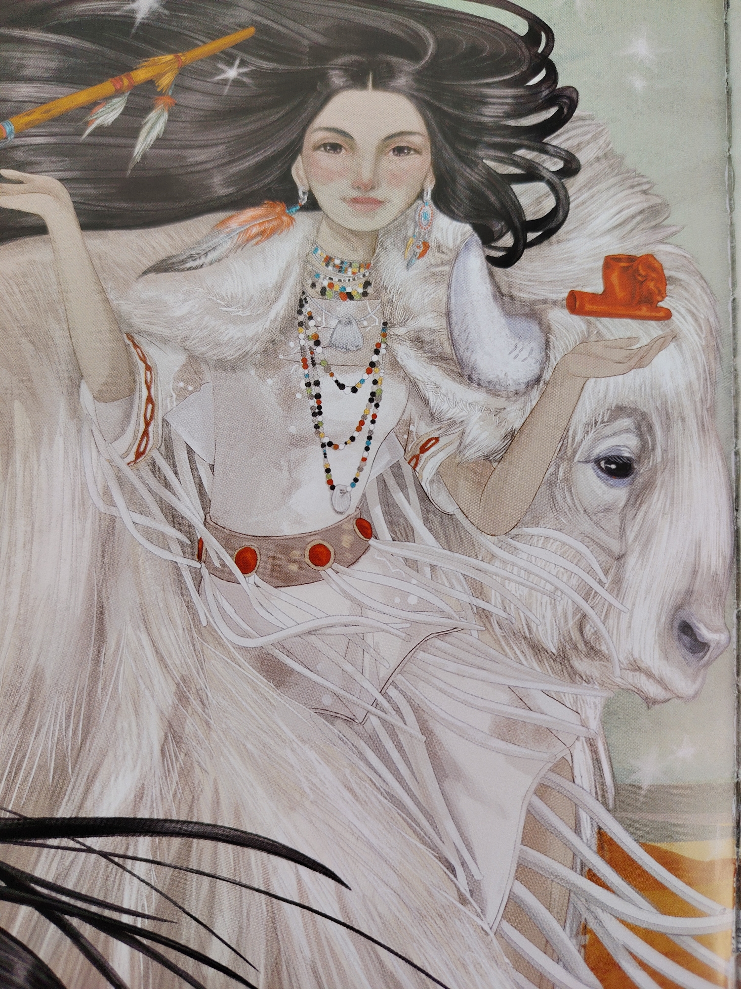 This is a watercolor illustration of a young woman with long, dark hair, adorned with colorful necklaces and earrings, standing beside a white bison. The woman is wearing a white robe with beaded detailing and a brown belt with red accents. She holds a wooden flute with feathers in her left hand and an orange object in her right hand, which is resting on the bison's head. The bison is depicted with its eye open, looking towards the viewer. The overall mood of the illustration is serene and mystical, with subtle star-like sparkles in the background suggesting a magical or spiritual theme. The artwork appears to be from a book or a similar publication, given the slightly rough edges of the image. There is no visible text in the image.