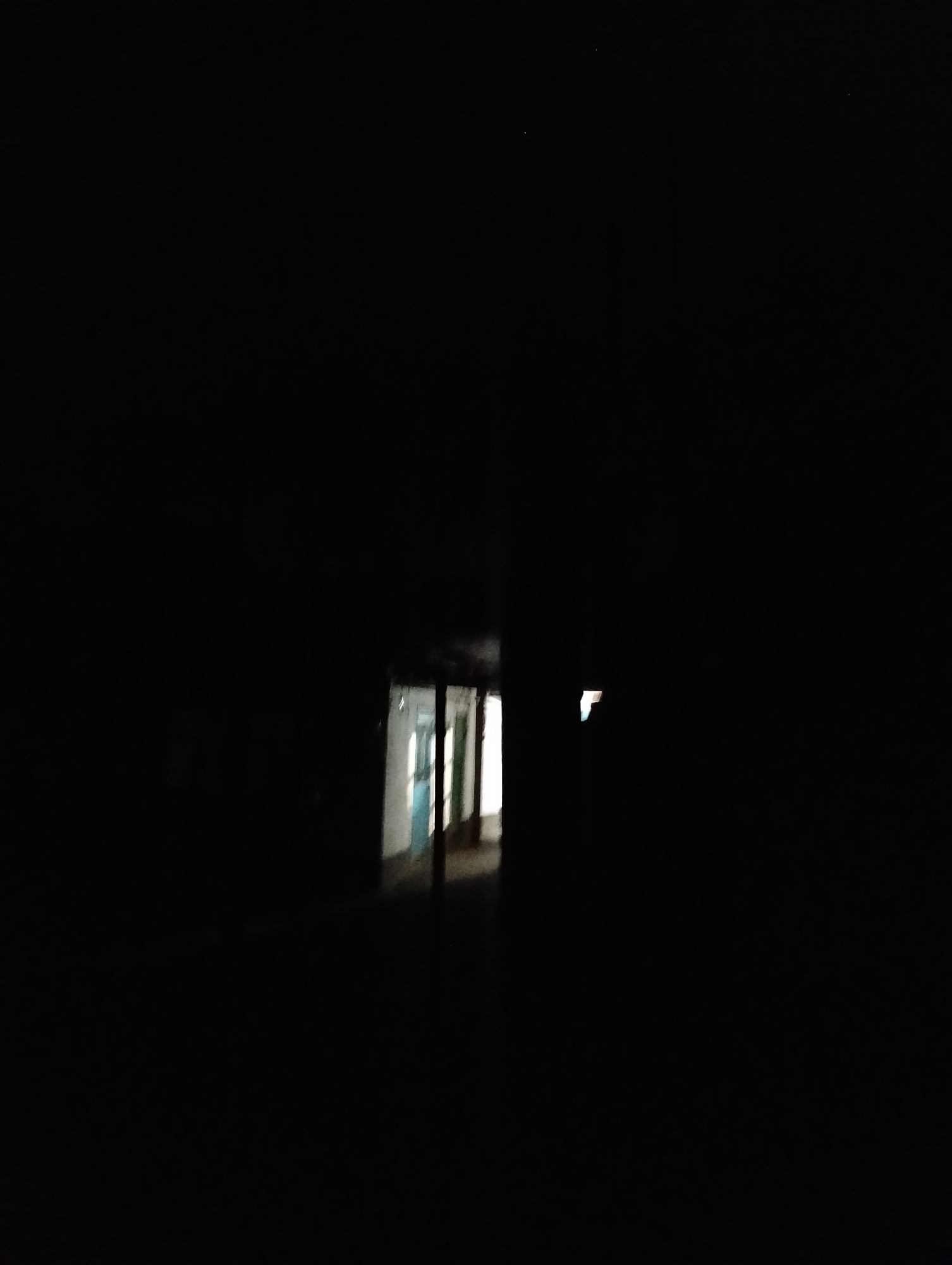 The image depicts a dark, narrow hallway with a faint light emanating from the end. The hallway appears to be part of an abandoned or disused building, possibly a school or dormitory, given the presence of what looks like lockers or cubbies along one side. The lighting suggests it is nighttime or the area is unlit. The scene evokes a sense of mystery and desolation. There is no visible text in the image. The location is identified as Қарғалы, Kazakhstan.