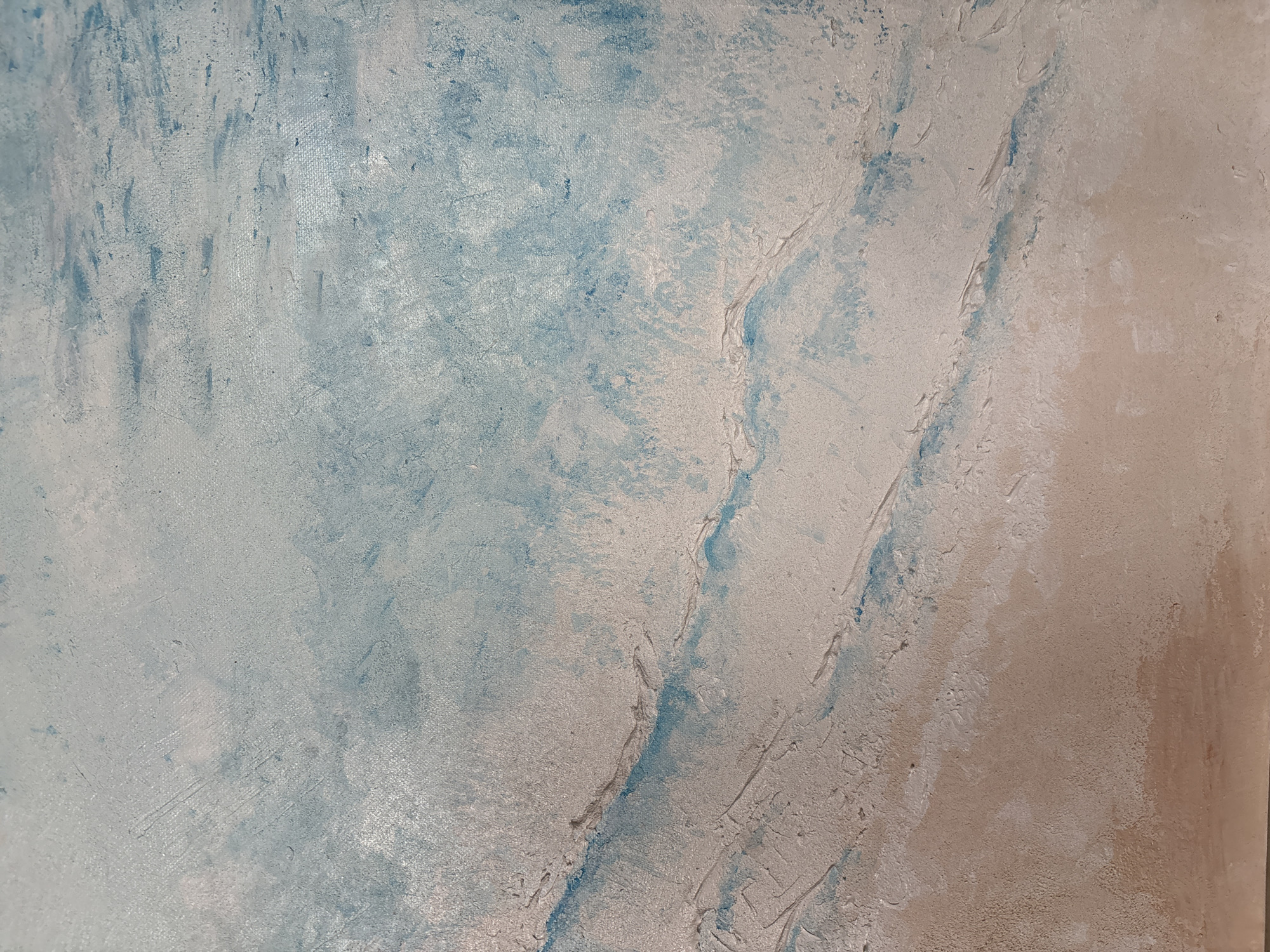 This is an abstract close-up image of a highly textured surface, likely a wall or an artistic canvas. The surface features a blend of colors: various shades of light blue and teal are prominent on the left and central parts, while a warm beige or tan hue dominates the right side. Off-white and light gray tones are also integrated throughout, particularly in the textured, raised areas.
The most notable detail is the pronounced three-dimensional texture. The surface appears uneven, with visible brushstrokes, grooves, ridges, and raised sections, suggesting the application of a thick medium such as paint, plaster, or stucco. These textural elements create an organic, fluid pattern, with streaks and swirls of blue paint cutting into the warmer beige areas. There is a general diagonal flow from the upper right to the lower left, influenced by the color distribution and textural lines.
No people, identifiable objects, or specific events are depicted in the image. The lighting is diffuse, highlighting the surface's tactile quality without strong shadows. The overall aesthetic suggests an aged, weathered, or intentionally distressed artistic finish. There is no visible text. The location context for this media file is Ulyanovsk, Russia.