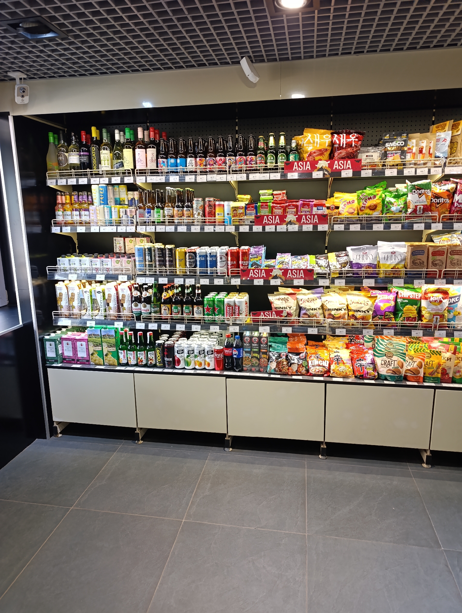 The image shows a shelf of products in a store. The shelves are stocked with various items including drinks, snacks, and bottled beverages. The products are neatly arranged on the shelves. The store appears to be well-lit and organized. The overall environment is that of a typical retail store or convenience store.