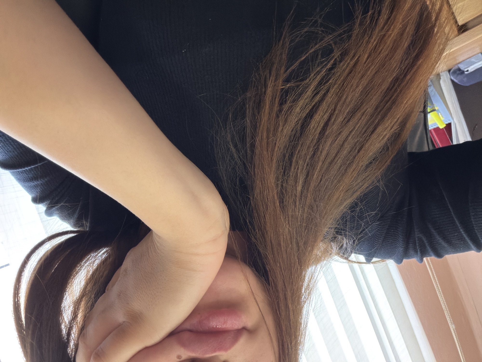 The image shows a close-up of a person's face and arm, partially obscured by their hand. The person has long, brown hair and is wearing a black, ribbed top. Their mouth is visible, and they appear to be resting their chin on their hand. The background consists of vertical blinds. The image was taken in Chișinău, Moldova.