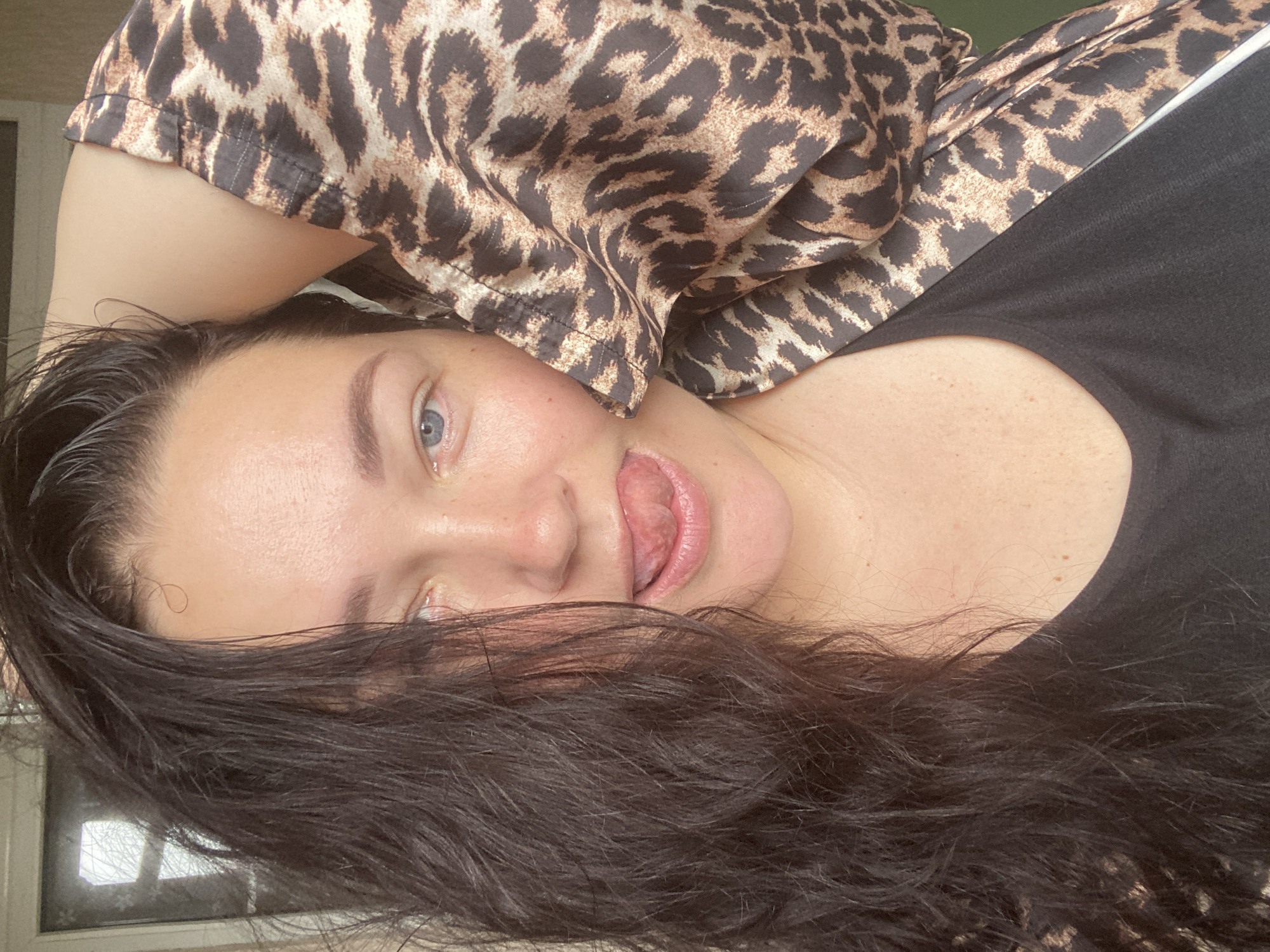 A person with dark hair is lying down, sticking their tongue out. They are wearing a leopard-print top and a black shirt underneath. The location is not discernible as being in Sochi, Russia, based on the visual information.