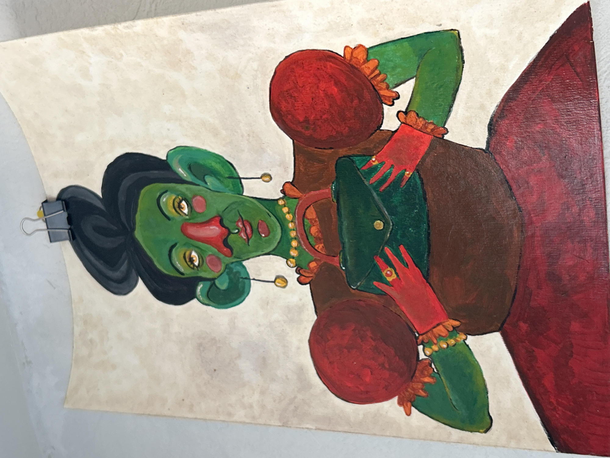 The image shows a painting of a green-skinned woman. Her hair is black and styled in a bun. She has red cheeks and nose and is adorned with a golden necklace and earrings. She is wearing red gloves and bracelets. The background of the painting is a mottled off-white. A portion of a red dress is visible on the right side of the painting. A binder clip is attached to the top left corner.