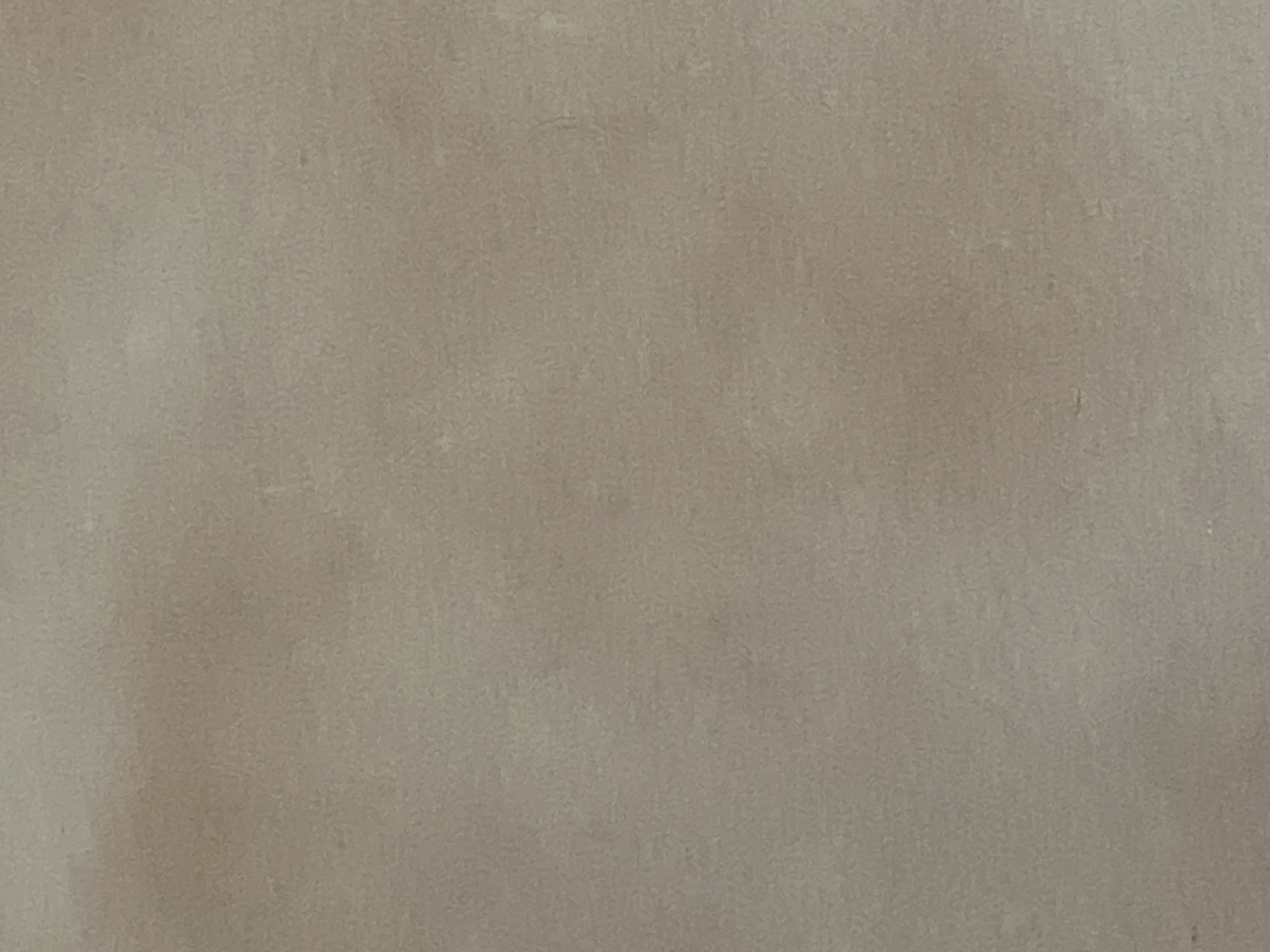 This is a close-up, top-down, eye-level shot of a textured, light beige or taupe surface. The surface appears to be a wall, possibly finished with plaster or a similar material, showing subtle variations in tone and texture. There are no discernible objects, people, or actions visible in the image. The lighting is diffused, creating soft shadows and highlights across the surface, giving it a slightly mottled appearance. The overall impression is one of a neutral, textured background. Given the nature of the image, it is not possible to determine its location within Casablanca, Morocco.