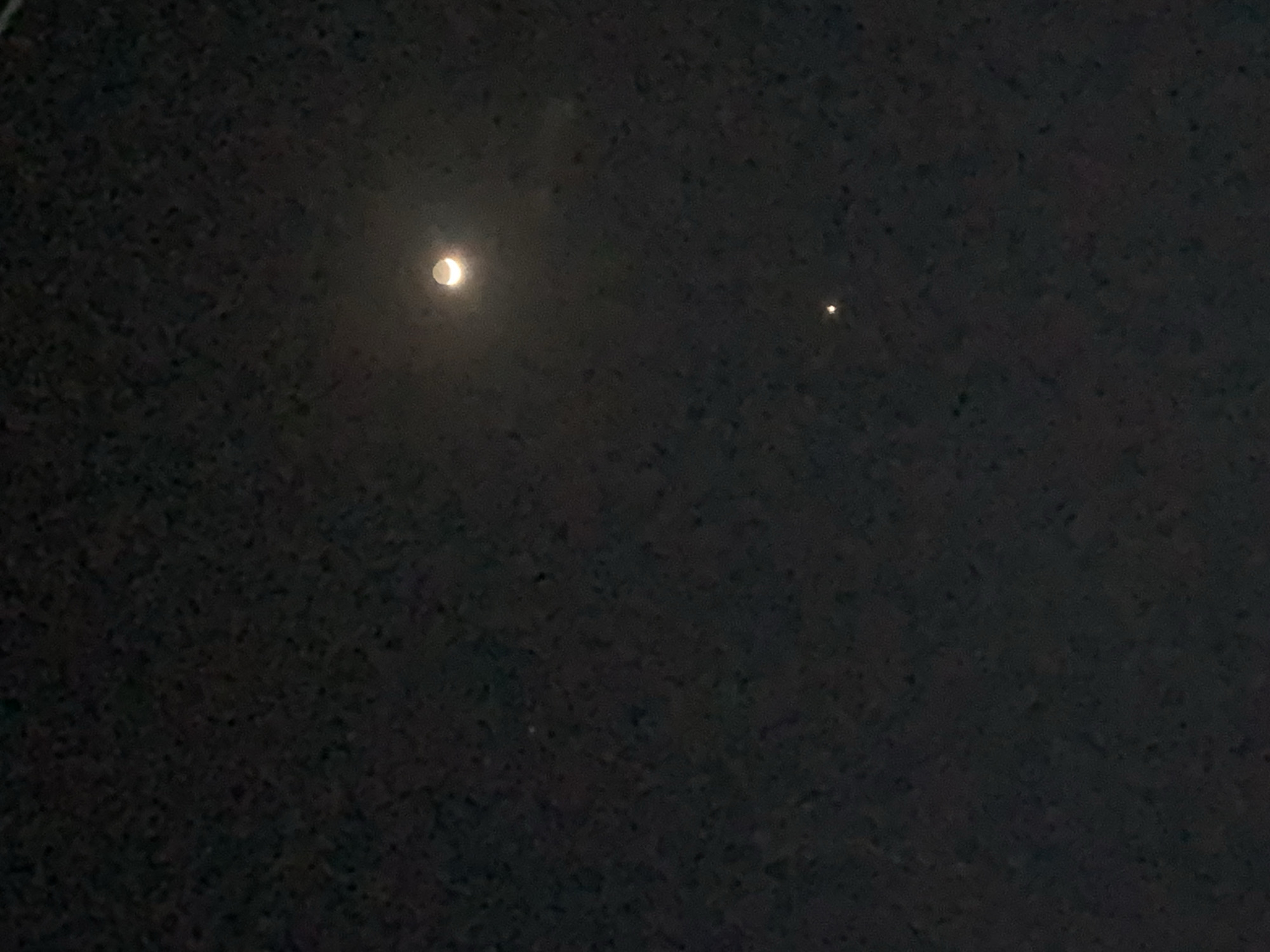 The image depicts a night sky. A crescent moon is visible on the left side, and a single, smaller point of light, possibly a star or planet, is seen on the right. The rest of the image is filled with darkness, indicative of a night scene. There is no information to determine if the image was taken in Kabong, Nigeria or anything about people, subjects, objects, or actions.