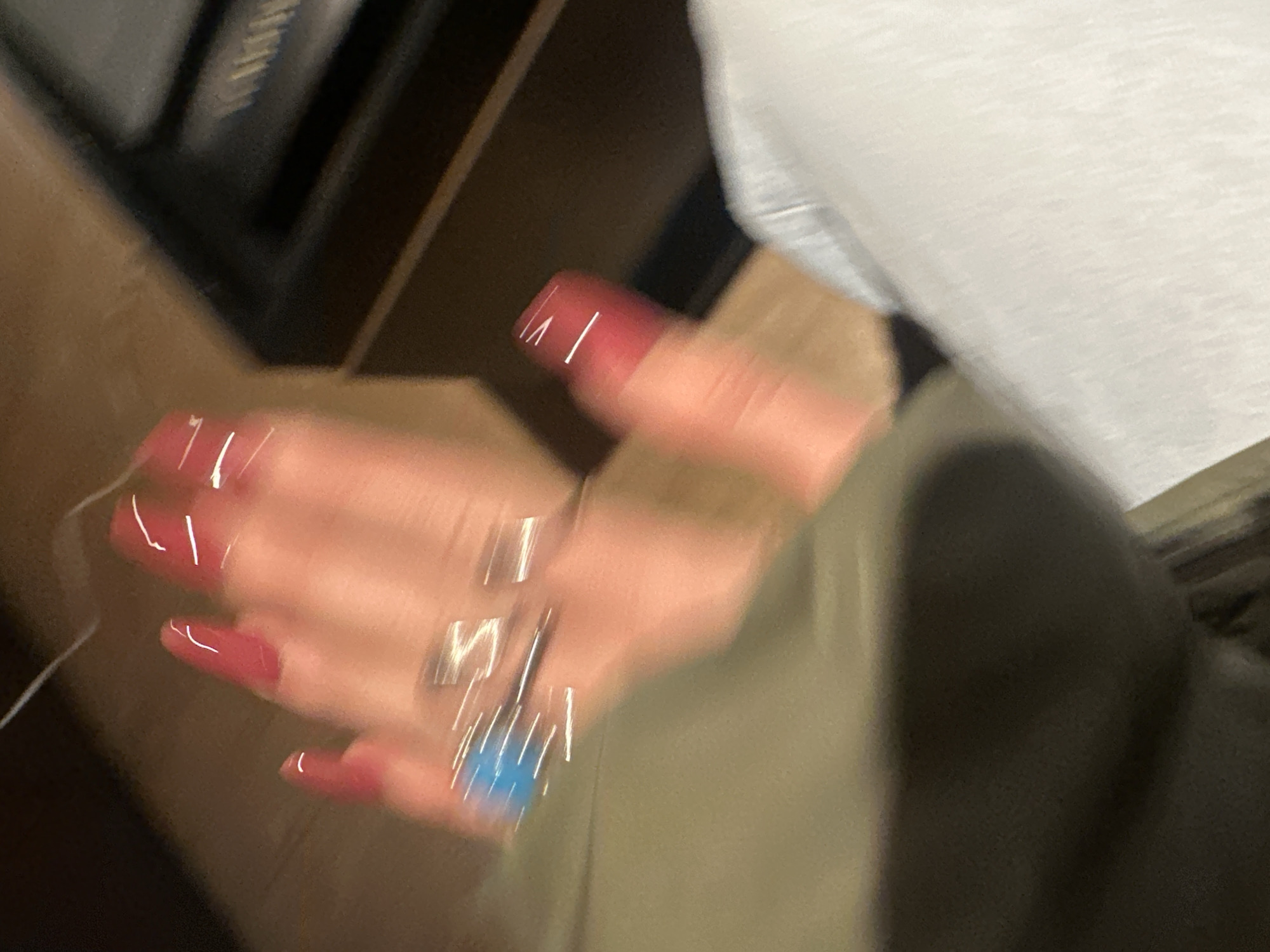 A blurry image shows a hand with red nail polish wearing a silver ring with a blue stone. The person appears to be wearing a white shirt and an olive green jacket. The background is dark. The location, Huixquilucan de Degollado, Mexico is not identifiable in this image.