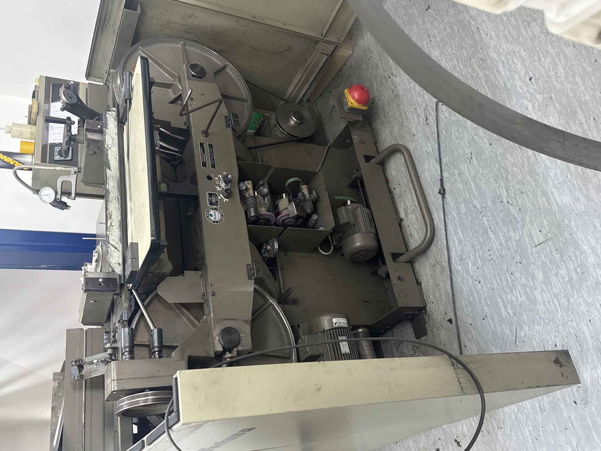 The image shows industrial machinery in what appears to be a workshop or factory setting. The machine is large and complex, with various mechanical components, gears, motors, and control panels. The machine is primarily composed of metal and appears to be functional, though some parts may show signs of wear. The surrounding environment is a floor with a light-colored, patterned surface, possibly linoleum or concrete with a coating. There are also some electrical cables and conduits visible. The lighting suggests an indoor environment, likely with artificial light sources. No people are present in the image. The location is identified as Vynnyky, Ukraine.