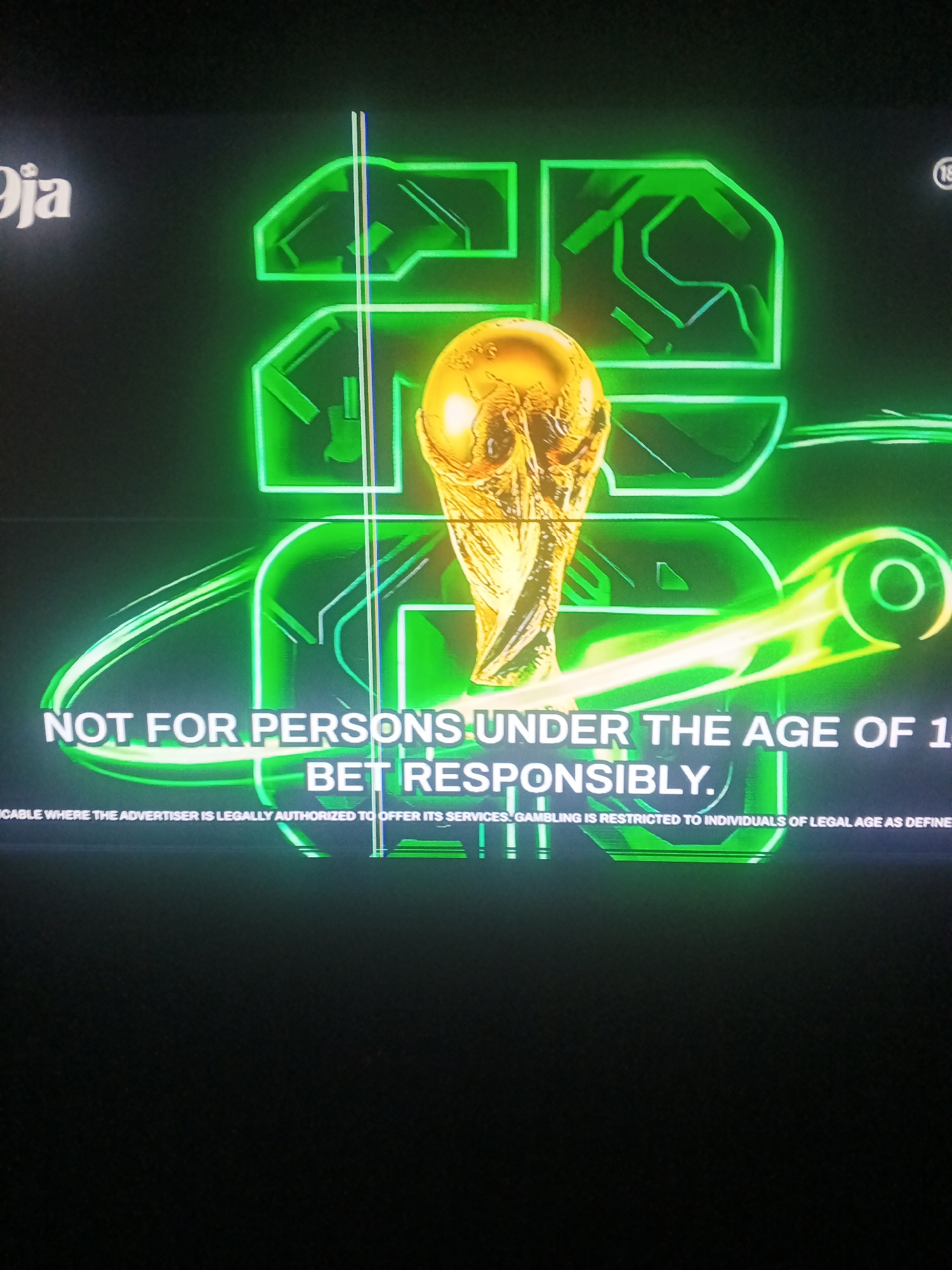 This media file appears to be a screenshot of an advertisement or a screen displayed during a broadcast. The central focus is a golden trophy, strongly resembling the FIFA World Cup trophy. Behind the trophy, there are large, neon green, abstract shapes that form what looks like the number "20" or stylized wings. To the left, there is white text that reads "Oja", and in the upper right corner, a circular emblem with the number "18" inside, indicating an age restriction.
Below the trophy and the neon shapes, there is prominent white text that reads: "NOT FOR PERSONS UNDER THE AGE OF 1 BET RESPONSIBLY." Further down, in smaller text, it states: "CABLE WHERE THE ADVERTISER IS LEGALLY AUTHORIZED TO OFFER ITS SERVICES GAMBLING IS RESTRICTED TO INDIVIDUALS OF LEGAL AGE AS DEFINE".
The overall aesthetic is dark with bright neon green and gold elements, suggesting a modern and perhaps energetic or exciting theme, likely related to sports betting or a similar service. There are no visible people or clear indications of a specific time of day or weather. The text suggests a gambling-related advertisement targeted at adults, emphasizing responsible gambling. The "Jalingo, Nigeria" context suggests this advertisement may have been displayed in that region.