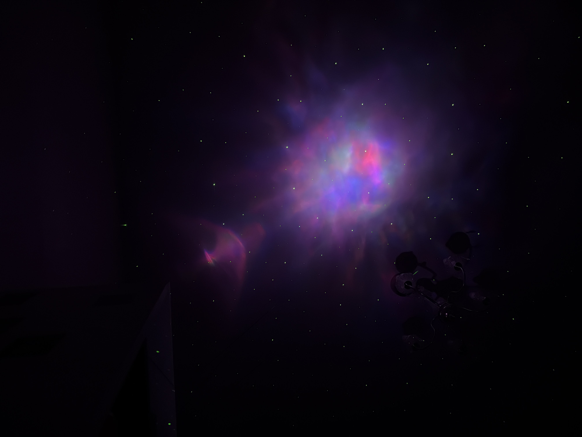 The image is of a purple and pink nebula in space, sparsely populated with faint green stars. A spacecraft appears in the bottom right, silhouetted against the nebula. A dark, sharp-edged object is visible in the lower left corner of the frame. There is no indication of the city of Perm, Russia.