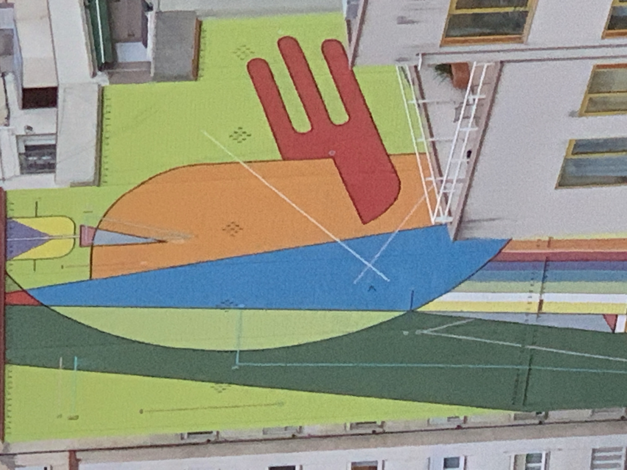 This is an aerial view of a building rooftop in Barcelona, Spain. The rooftop is covered with a colorful abstract mural consisting of geometric shapes and lines in shades of green, orange, blue, and red. A red, hand-like shape with three fingers is located in the upper portion of the mural. A white metal staircase is attached to the side of an adjacent building, partially overlapping the mural. Windows are visible on the side of the adjacent building. Other building elements are located on other sides of the mural.