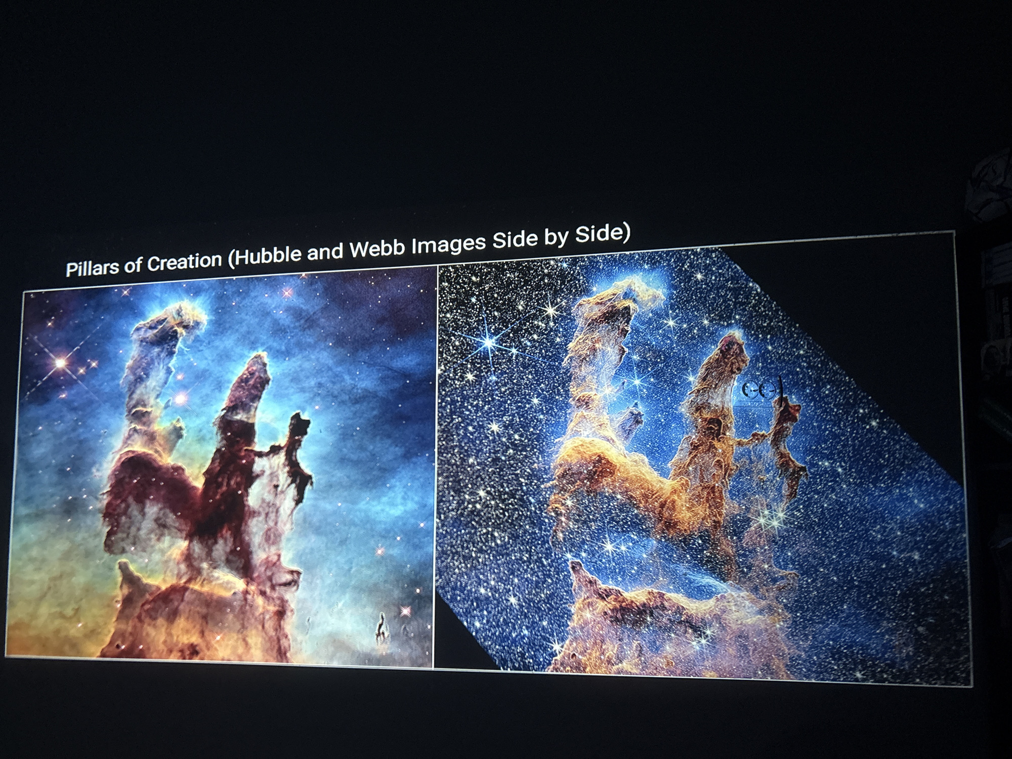 The image shows a side-by-side comparison of the Pillars of Creation as captured by the Hubble Space Telescope and the James Webb Space Telescope. The scene consists of two images displayed on a screen against a dark background.
The left image (Hubble) displays the pillars in a blue and red color scheme with fewer visible stars. The right image (Webb) is in a predominantly orange and blue palette, revealing many more stars. Both images show the same cosmic structures, but the Webb image exhibits greater clarity and detail due to its advanced infrared capabilities. The title reads: "Pillars of Creation (Hubble and Webb Images Side by Side)." The location is unknown.