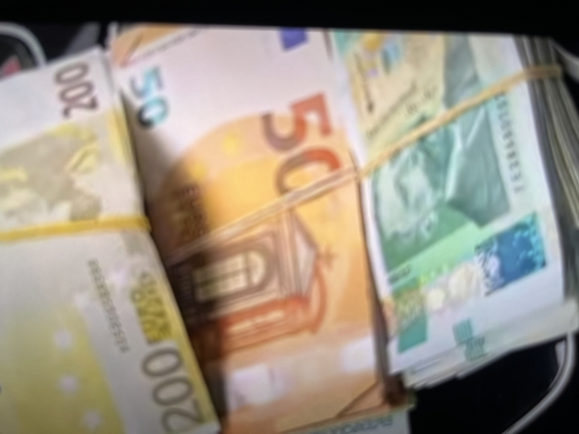 The image shows three bundles of Euro banknotes, secured with rubber bands. The denominations visible are 200 Euro, 50 Euro, and 20 Euro. The image appears to be taken indoors. There is no evidence to suggest that this image was taken in Elin Pelin, Bulgaria.