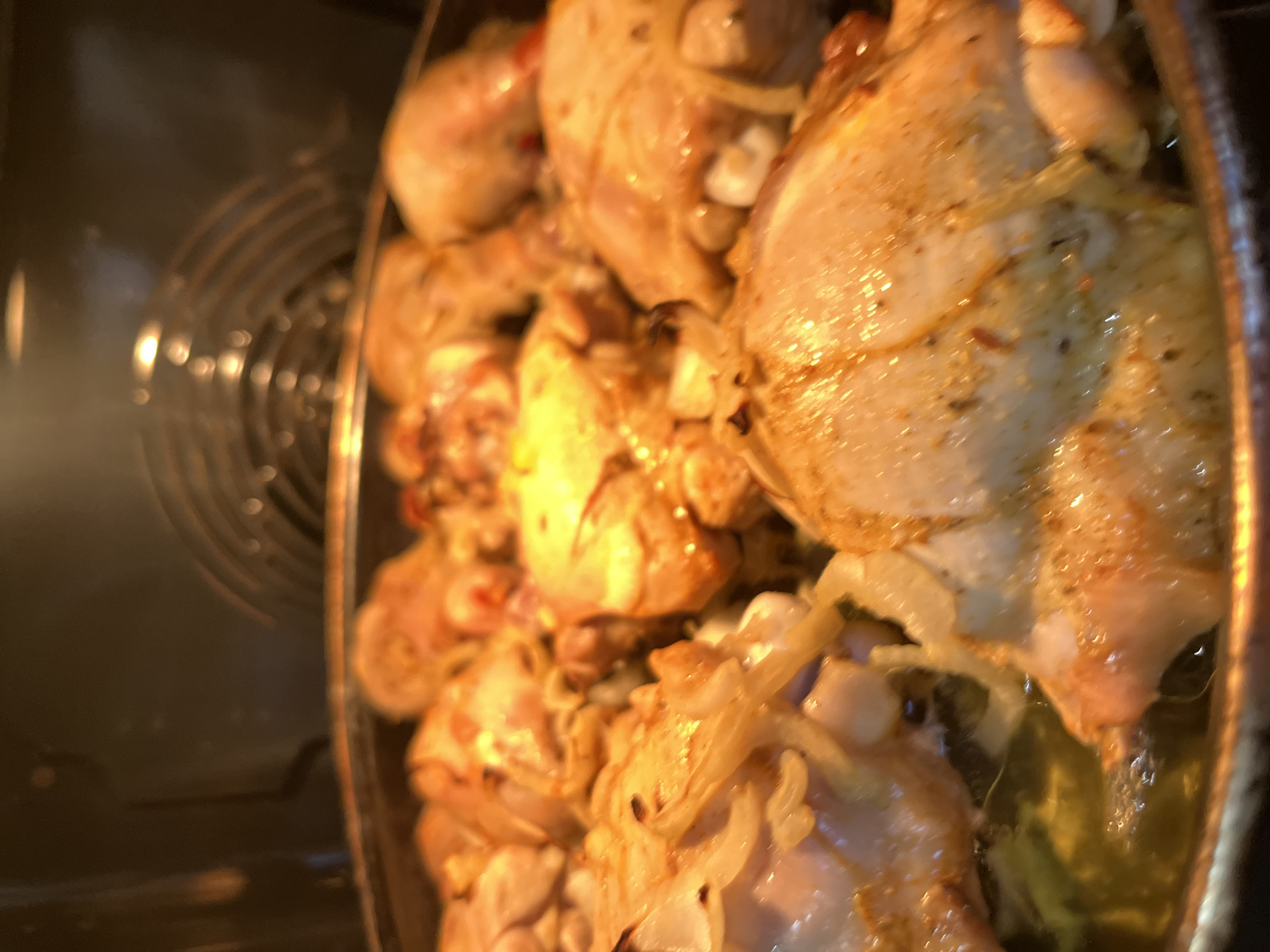 The image shows a metallic baking pan filled with cooked chicken pieces and onions, likely inside an oven. The chicken appears to be browned and seasoned. The oven's interior, including the heating element, is visible in the background. There is no indication of the location being Kaspiysk, Russia or any people in the image.