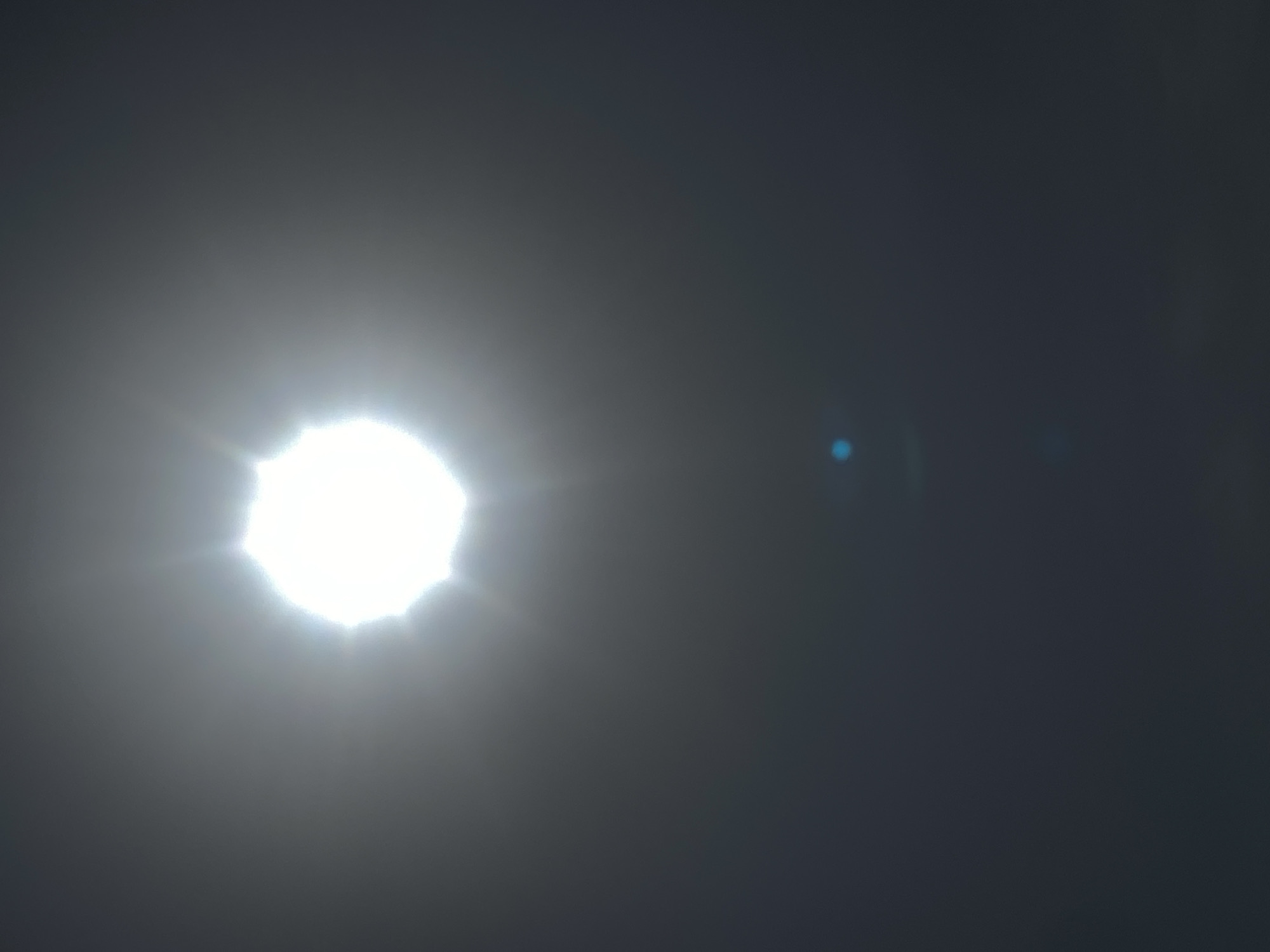 A bright light source, likely the sun, dominates the left side of the frame. A lens flare is visible on the right. The overall ambient lighting is dim, suggesting a twilight or overcast sky. The location is unknown, I cannot provide a city or country of the picture.