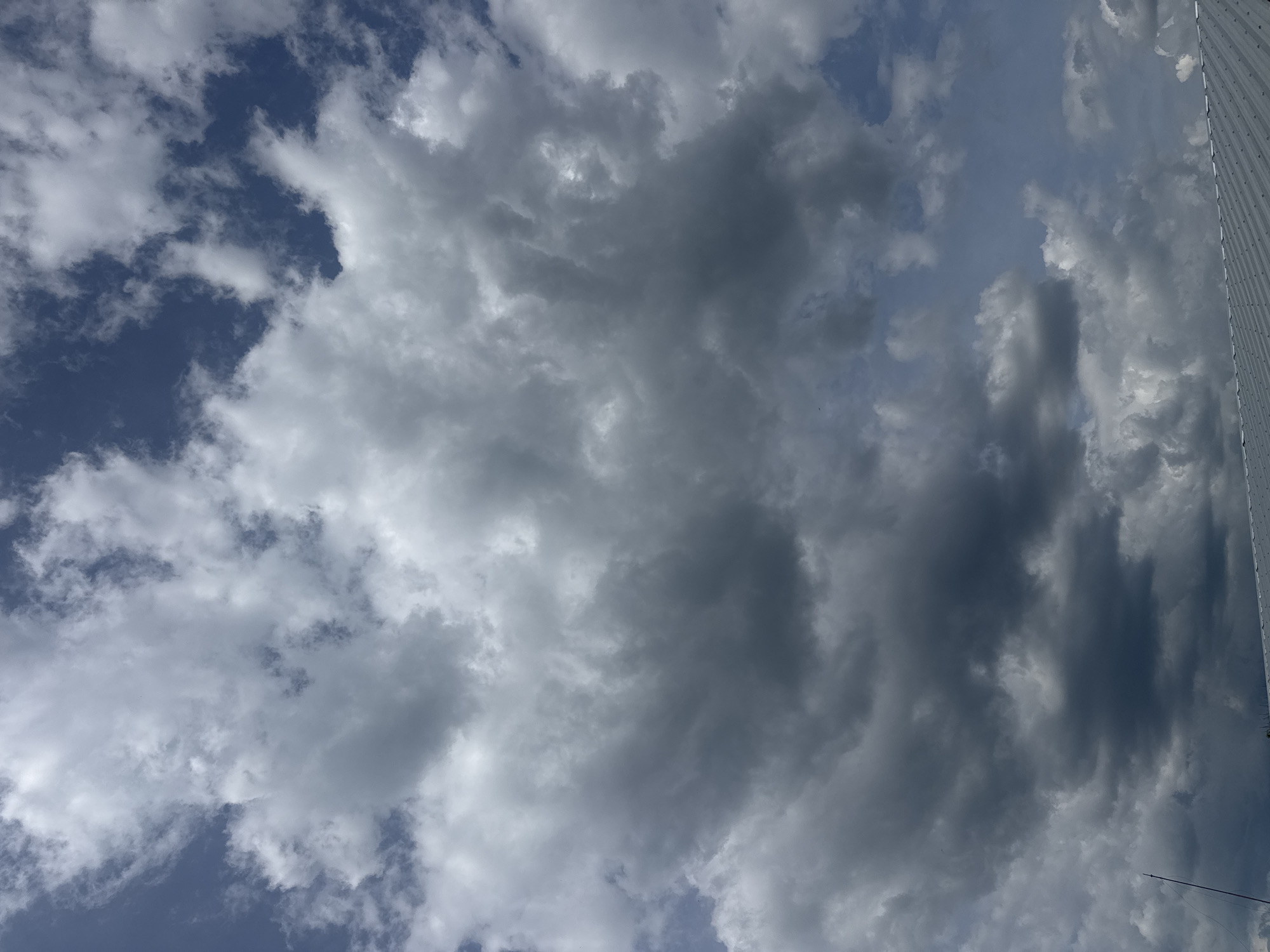 The image depicts a sky filled with a mixture of dark gray and white clouds. Patches of blue sky are visible between the clouds. A portion of a corrugated metal structure is visible on the right edge of the frame. The location is Sarnevo, Bulgaria.