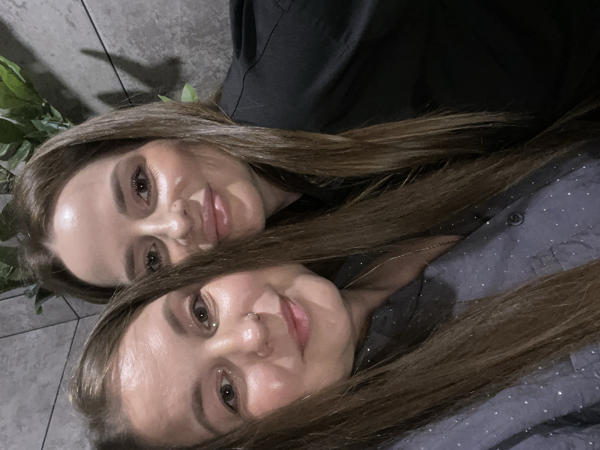 Two women pose close together. The woman on top is wearing a black shirt, and the other woman is wearing a dark shirt with small white dots. Both women have brown hair. The location is not identifiable as Izhevsk, Russia, based on the image.