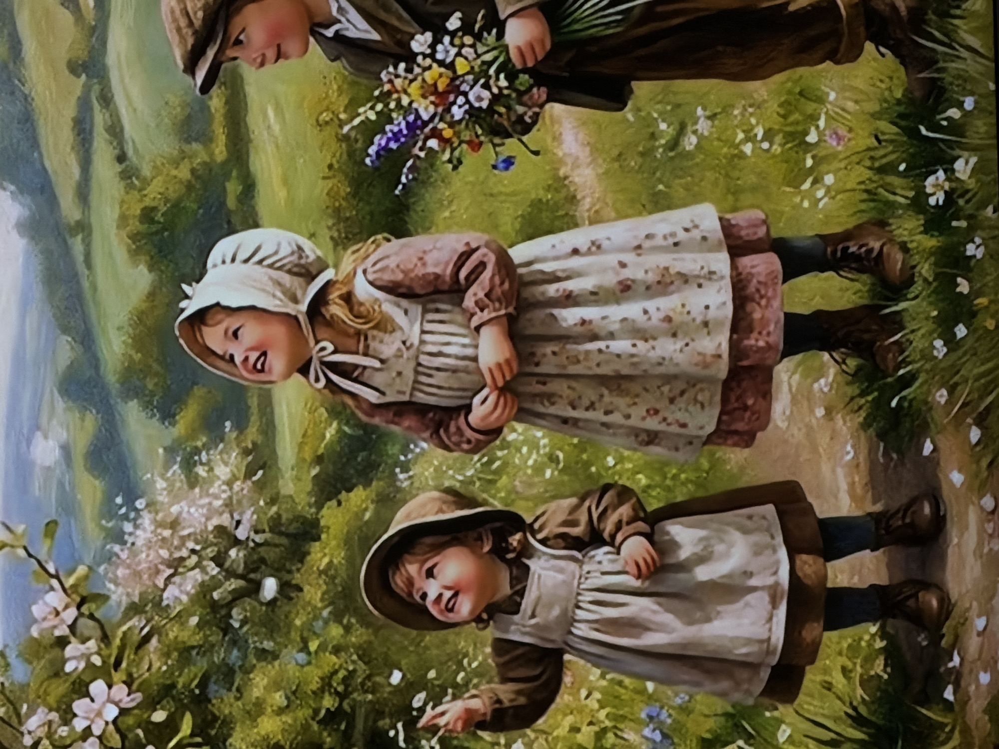 This is a painted image depicting three children enjoying a sunny day in a lush, green rural landscape, possibly in the region of Sofiivska Borshchahivka, Ukraine. The artwork has a soft, pastoral aesthetic.
At the top, a boy in a brown cap and dark clothing holds a vibrant bouquet of wildflowers, including purple, yellow, and white varieties. He looks down towards the two girls.
Below him, a young girl with blonde hair, wearing a white bonnet and a long-sleeved dress with a floral-patterned apron, smiles warmly as she looks up and to her left. She wears dark boots.
At the bottom of the frame, a smaller girl, also smiling, wears a brown hat and a similar dress and apron combination. She extends her right hand forward, seemingly reaching out or observing something in front of her, perhaps petals from a nearby flowering bush.
The children are positioned on or near a narrow, light-colored dirt path that winds through verdant grass. The ground is dotted with numerous small white and blue wildflowers. Flowering bushes with light pink or white blossoms are visible on the left, adding to the serene natural setting. The background features rolling green hills under a bright, implied sky.
The scene conveys a sense of innocence, joy, and peaceful exploration of nature. The children's expressions are happy, and the overall atmosphere is tranquil and idyllic. The time of day appears to be daytime, with soft, ample light. No visible text is present in the image.