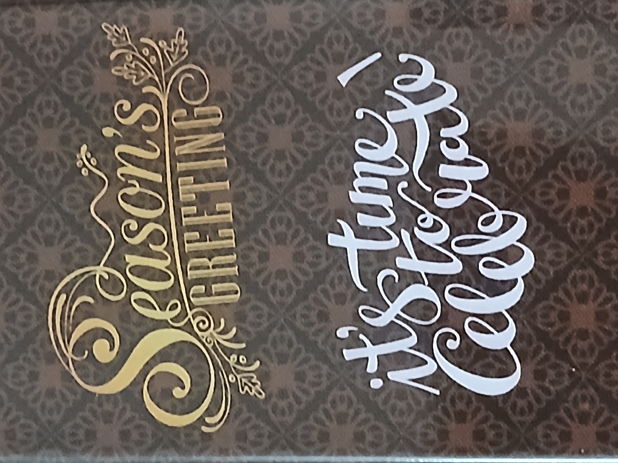 The image shows a dark brown surface with a repeating floral pattern. On the left, in gold lettering, is "Season's Greetings" with decorative flourishes. On the right, in white lettering, is "It's time to celebrate!". The location of Bengaluru, India is not evident from the image content.