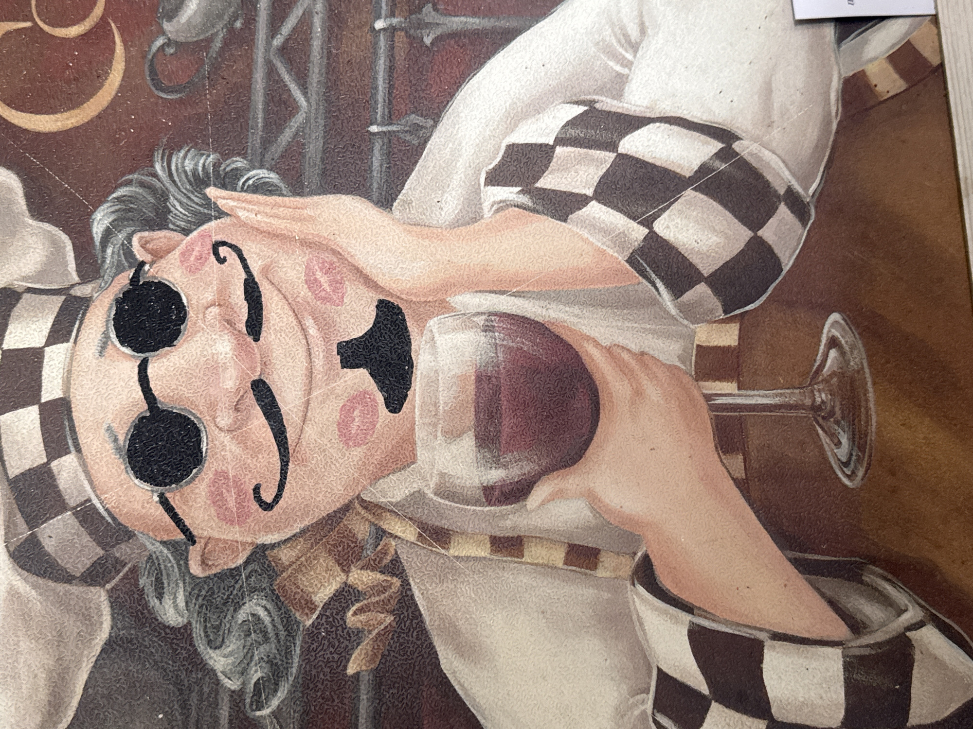 The image is a close-up of a painting depicting a cartoonish chef. The chef has gray curly hair, round black sunglasses, a thin mustache, and red lipstick marks on his cheeks and chin. He is wearing a chef's hat with a checkered pattern, a white chef's coat, and an apron. He is holding a wine glass filled with red liquid in his right hand and resting his left hand on his cheek. The background is dark and textured, with some blurry elements suggesting shelves and kitchen equipment. There is no indication of the city of Zaokskiy, Russia in this image.