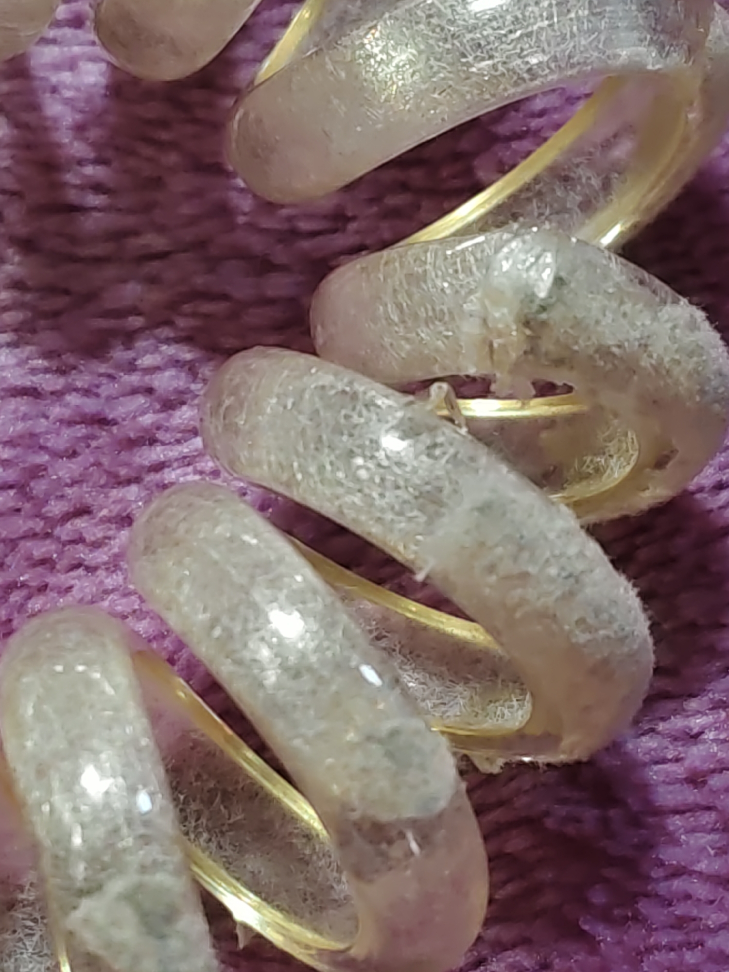 The image shows a close-up, macro shot of several coiled objects with a golden core wrapped in a translucent, textured material. These coiled objects are lying on a purple, textured surface, possibly fabric or carpet. The lighting creates reflections and highlights on the coiled objects, emphasizing their texture and the sheen of the golden core. There are no people or identifiable landmarks visible in the image. The scene appears to be an indoor, still life composition.
