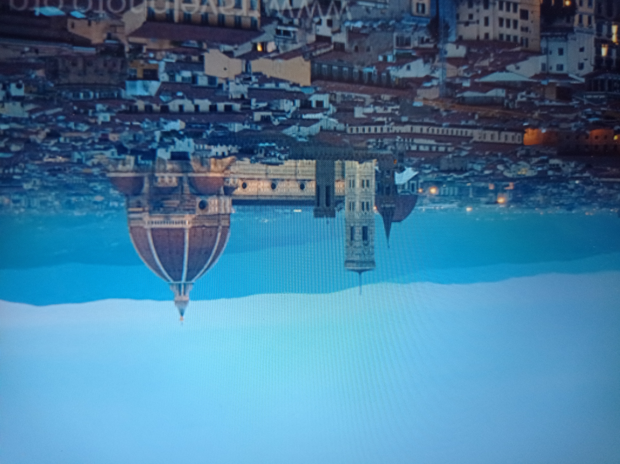 The image is a digital photograph of a cityscape at dusk or dawn. The dominant features are a large cathedral with a prominent dome and a bell tower, characteristic of Italian Renaissance architecture. The cathedral is surrounded by a dense urban environment composed of many buildings with terracotta roofs. In the background, hazy blue mountains are visible against a pale blue sky. The lighting suggests twilight. There are no people visible in the image. The scene depicts a historic European city, likely Florence, Italy, given the architectural style. The provided information about Mukachevo, Ukraine is inaccurate for this image.